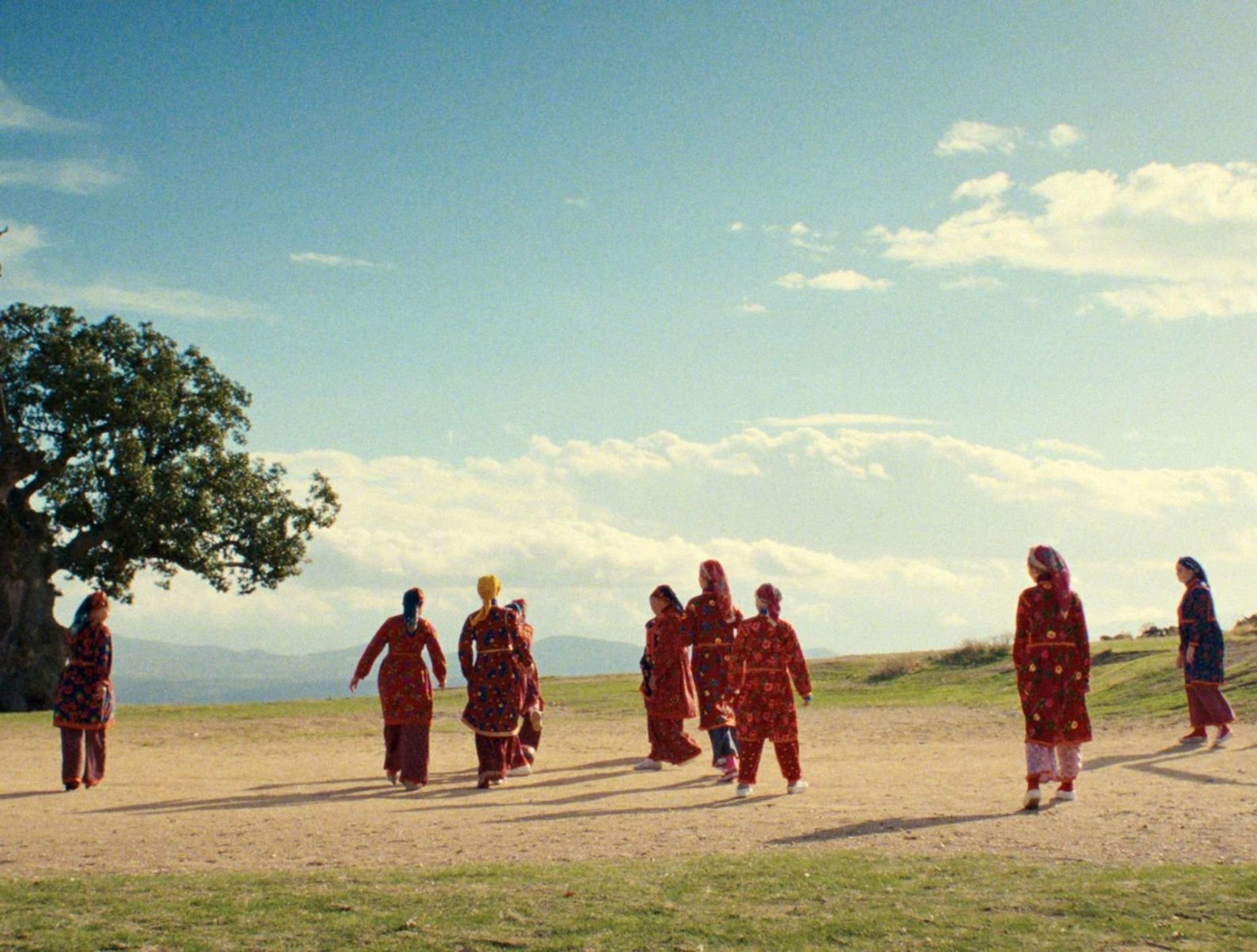 Frauen in traditionellen roten Kleidern gehen auf einem Feld unter blauem Himmel.