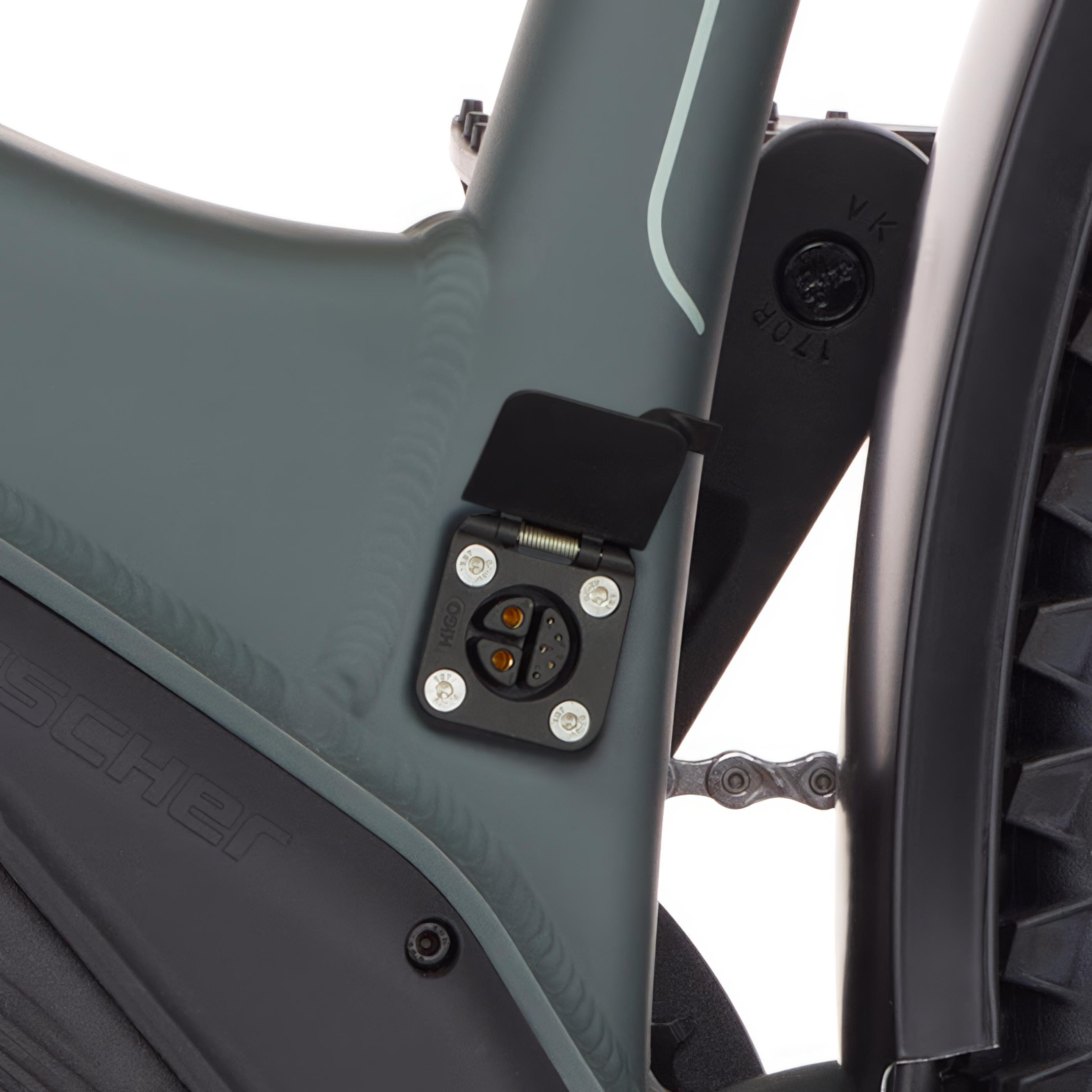Nahaufnahme des Ladeanschlusses eines grauen E-Bikes mit Kette und schwarzem Schutzblech.