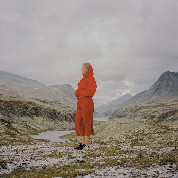 Frau in rotem Outfit steht in bergiger Landschaft mit See.