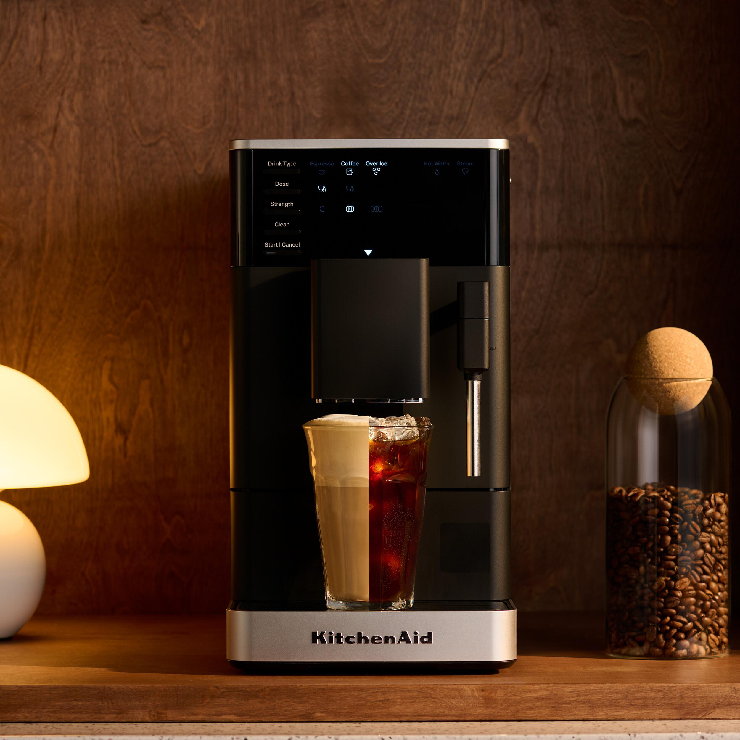 Kaffeemaschine brüht ein Getränk in ein Glas mit Eis und Milchschaum.
