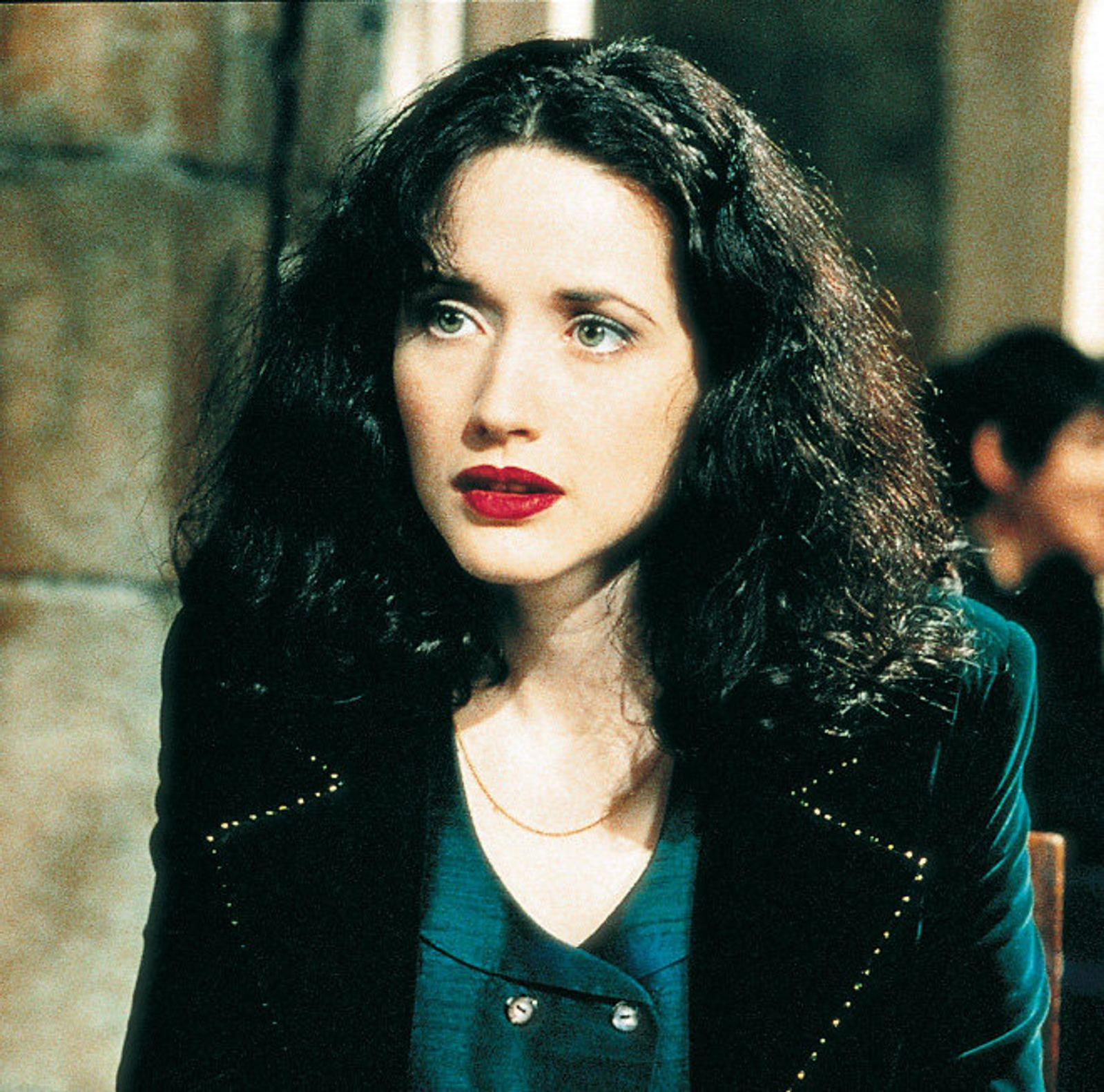 Eine Frau mit dunklem Haar und rotem Lippenstift, die einen schwarzen Blazer trägt.