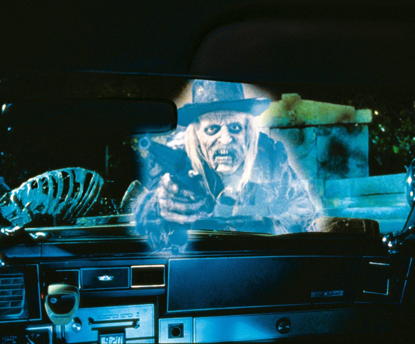Ein Geist mit Hut und Waffe fährt in einem Auto, dessen Armaturenbrett sichtbar ist.