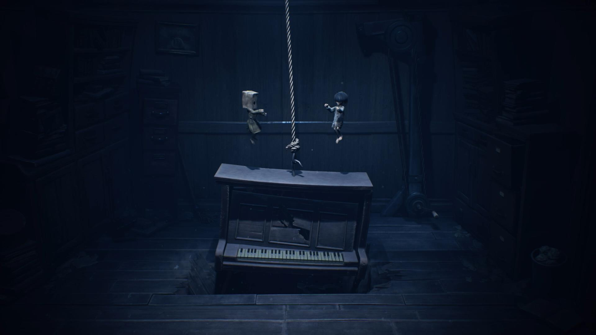 Zwei Kinder hängen an einem Seil über einem zerbrochenen Klavier in einem dunklen Raum.
