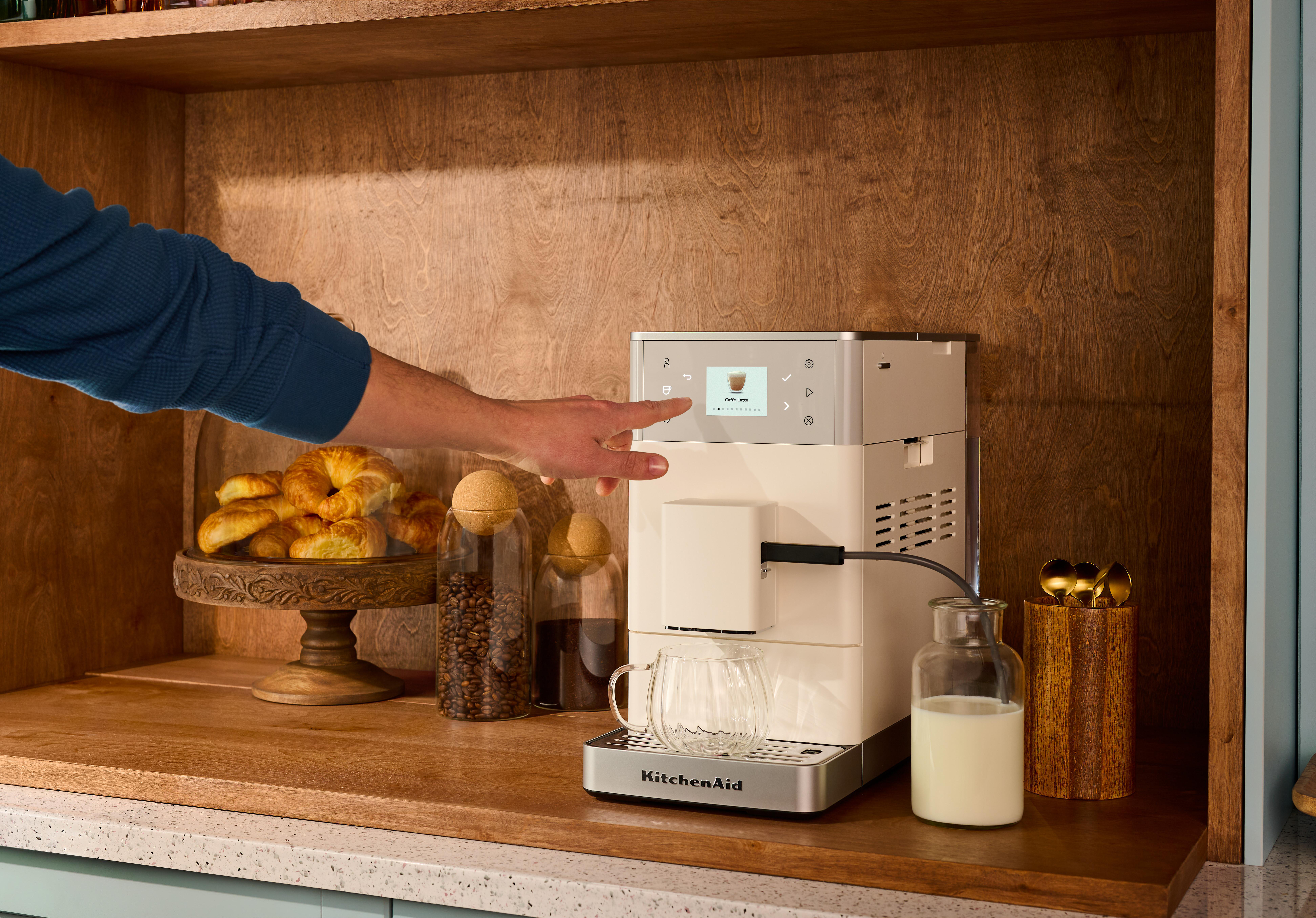 Mann bedient Kaffeemaschine mit Touchscreen. Croissants, Kaffee, Milch und Tassen auf der Theke.