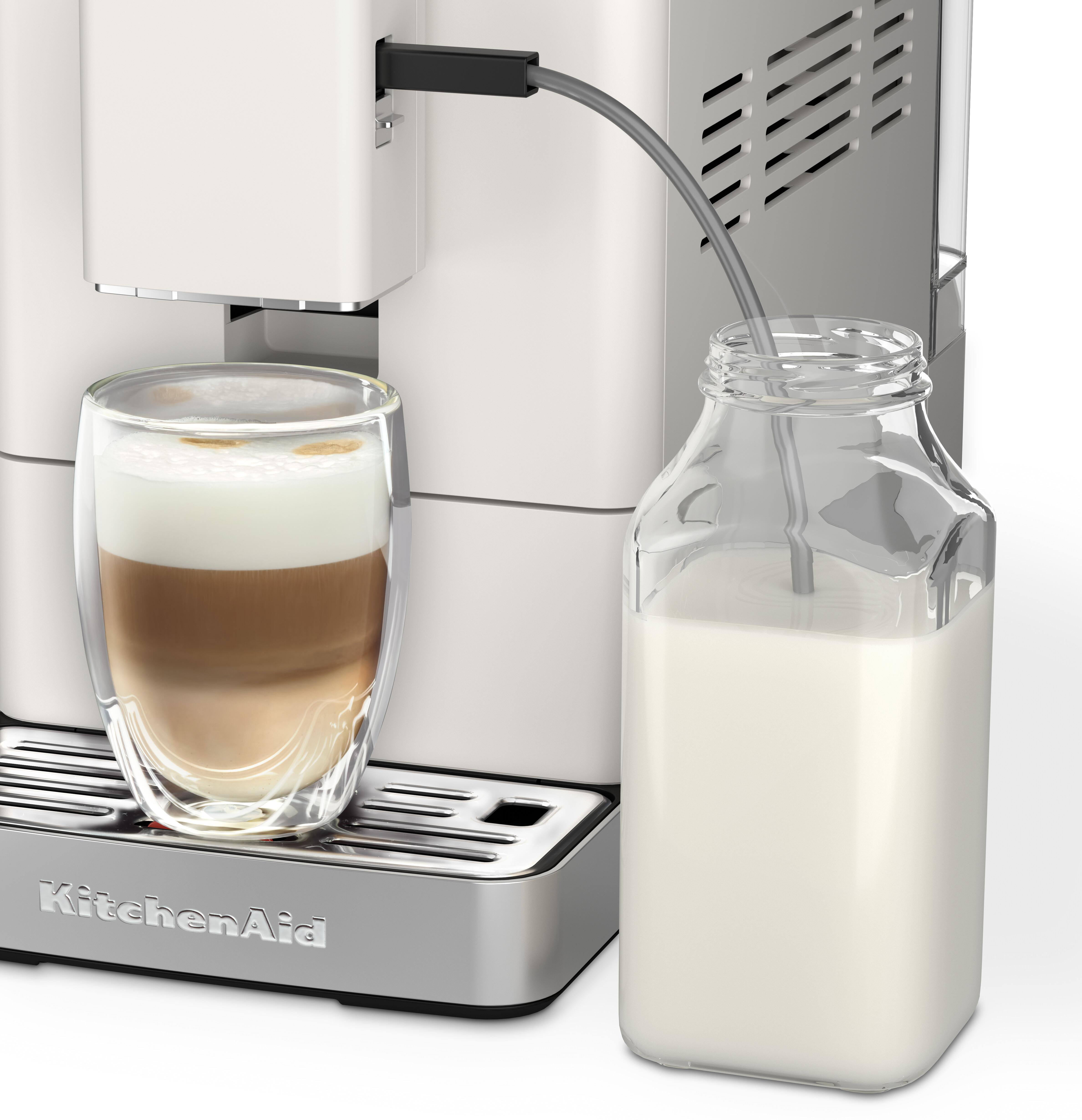 Eine weiße Kaffeemaschine mit einem Glas Latte und einer Milchkaraffe daneben.