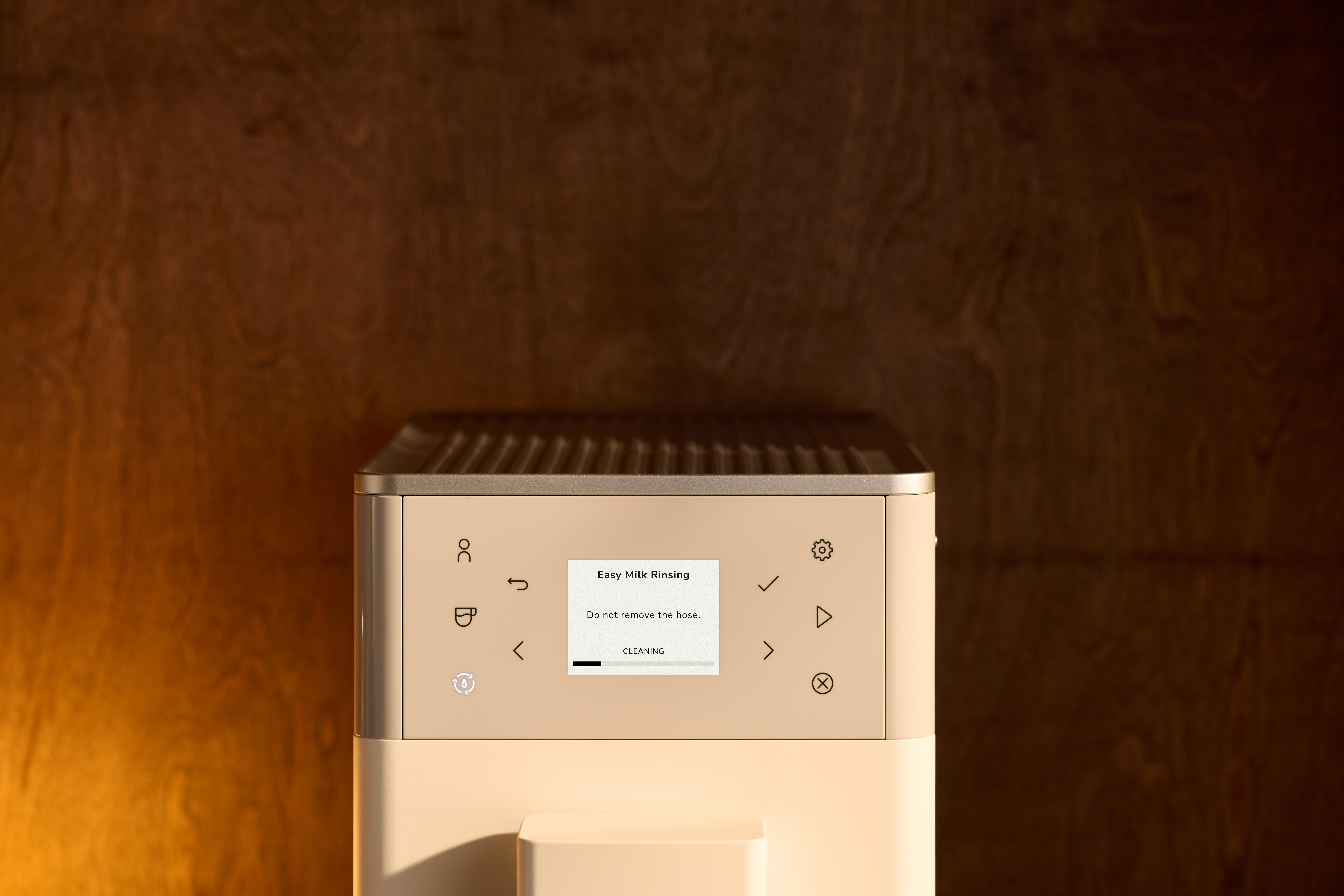 Kaffeemaschine mit Display zeigt Milchspülung an, Hintergrund Holz.