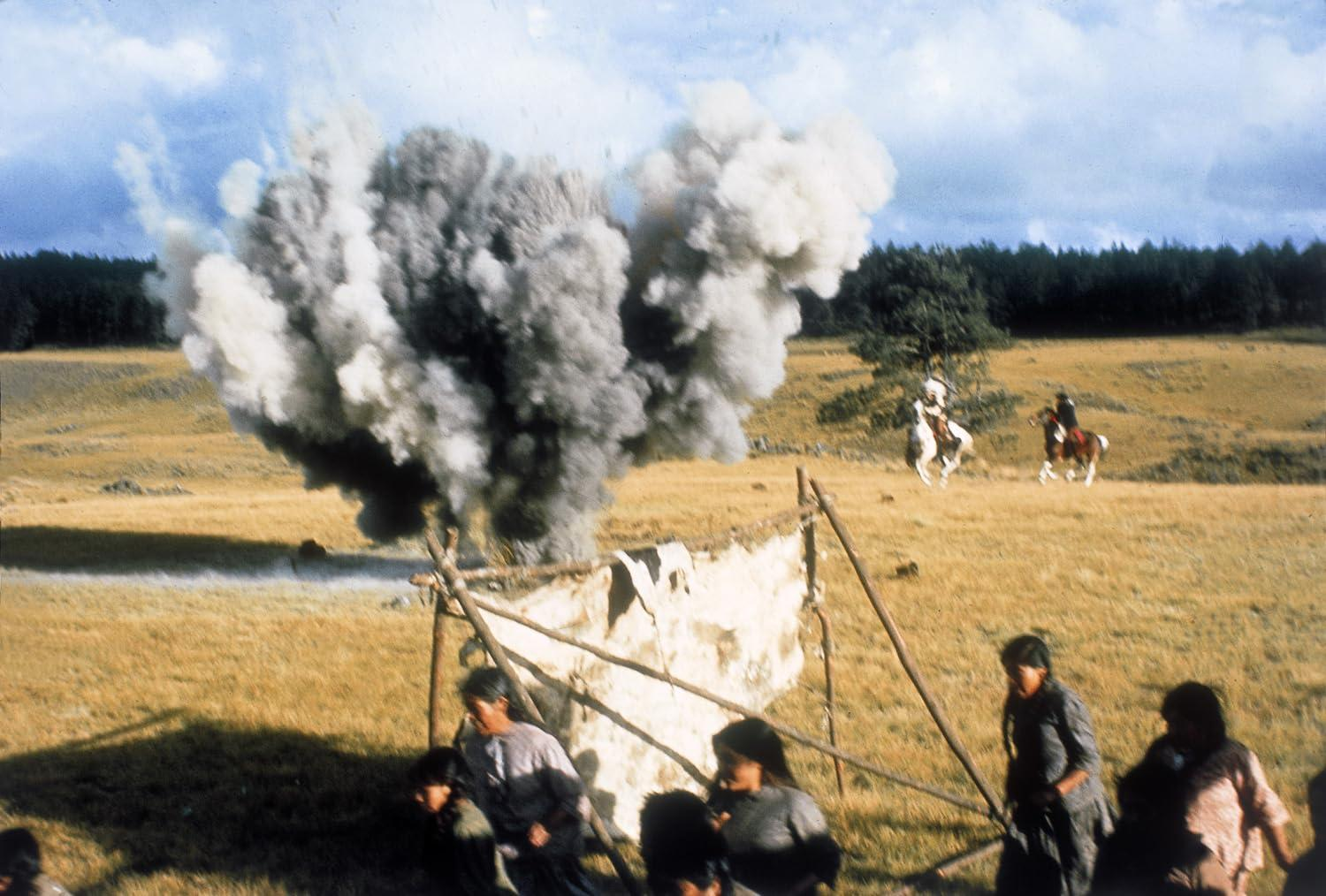 Explosion mit Rauchwolken über einem Feld, Reiter im Hintergrund, Menschen in Vordergrund.