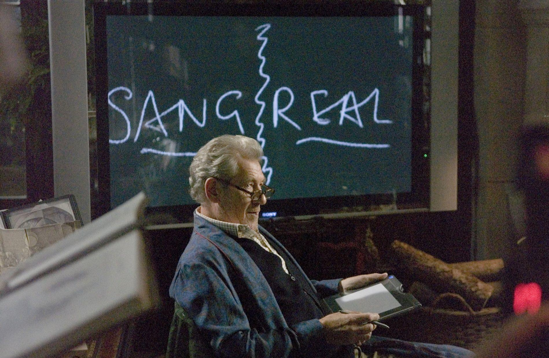 Ein älterer Mann sitzt und hält ein Tablet. Auf dem Bildschirm steht in weißer Schrift SANG REAL.