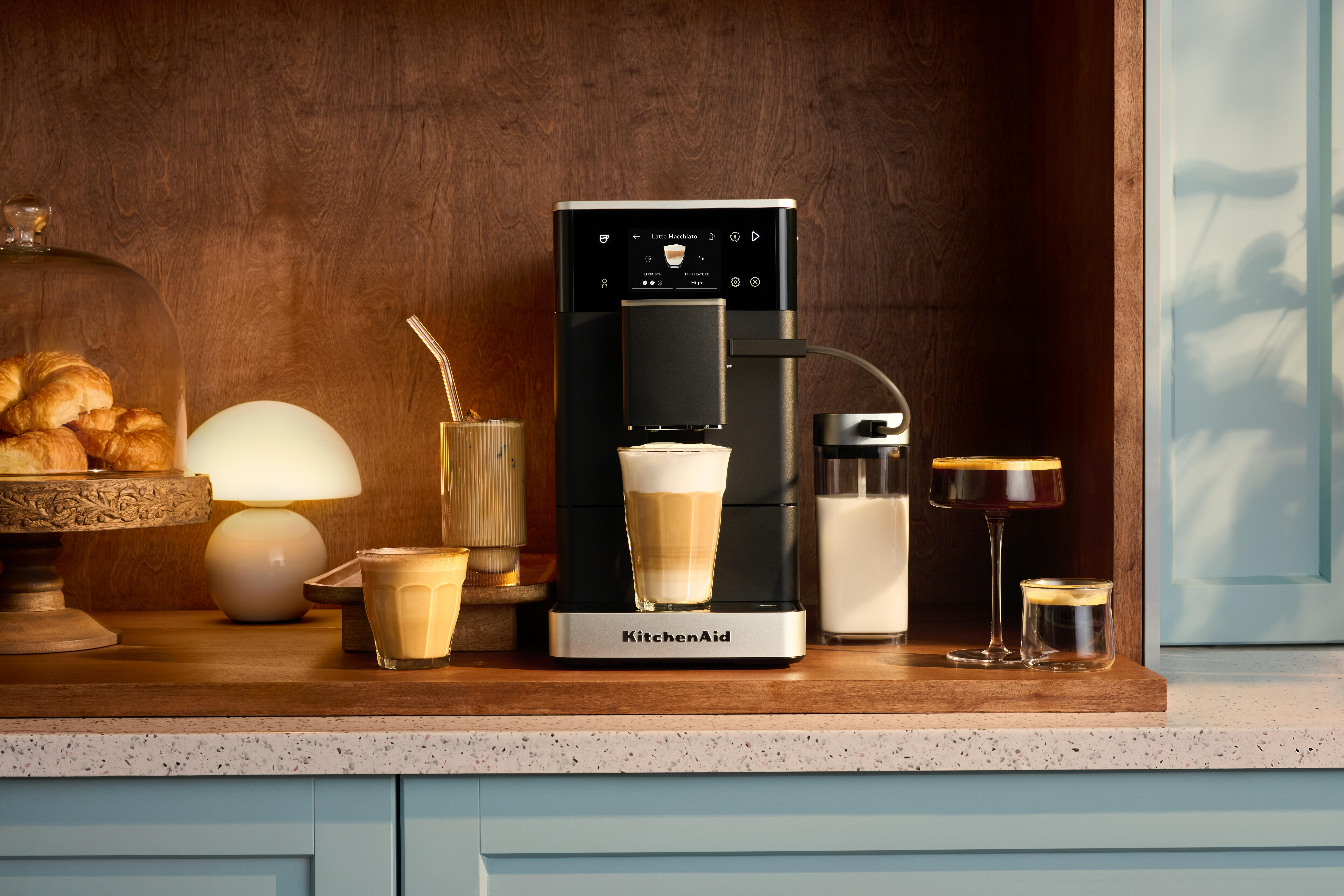 Kaffeemaschine mit Milchkaraffe und Kaffeegetränken auf einem Holztresen.