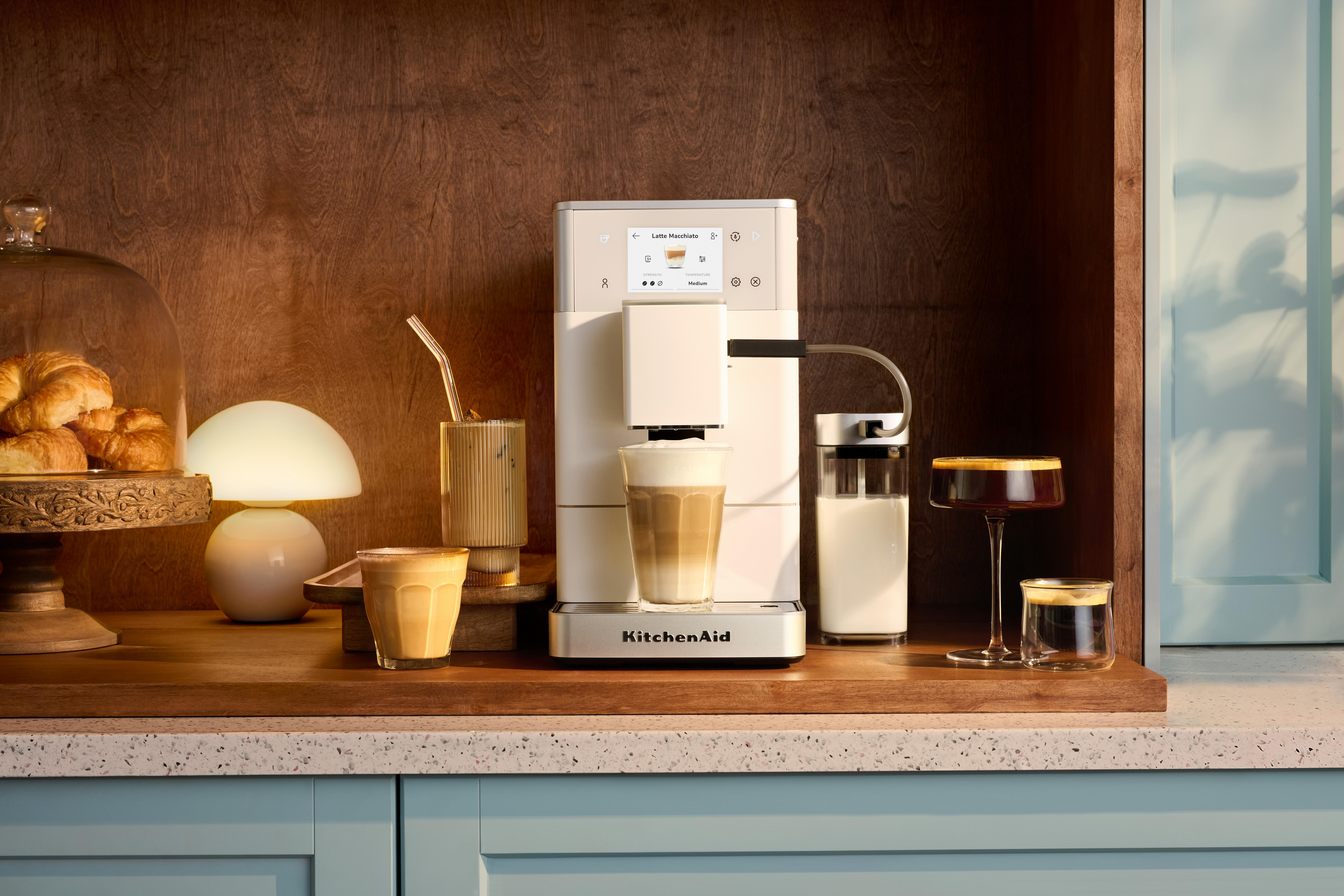 Eine Kaffeemaschine macht einen Latte Macchiato neben Croissants, einer Lampe und Kaffeegetränken.