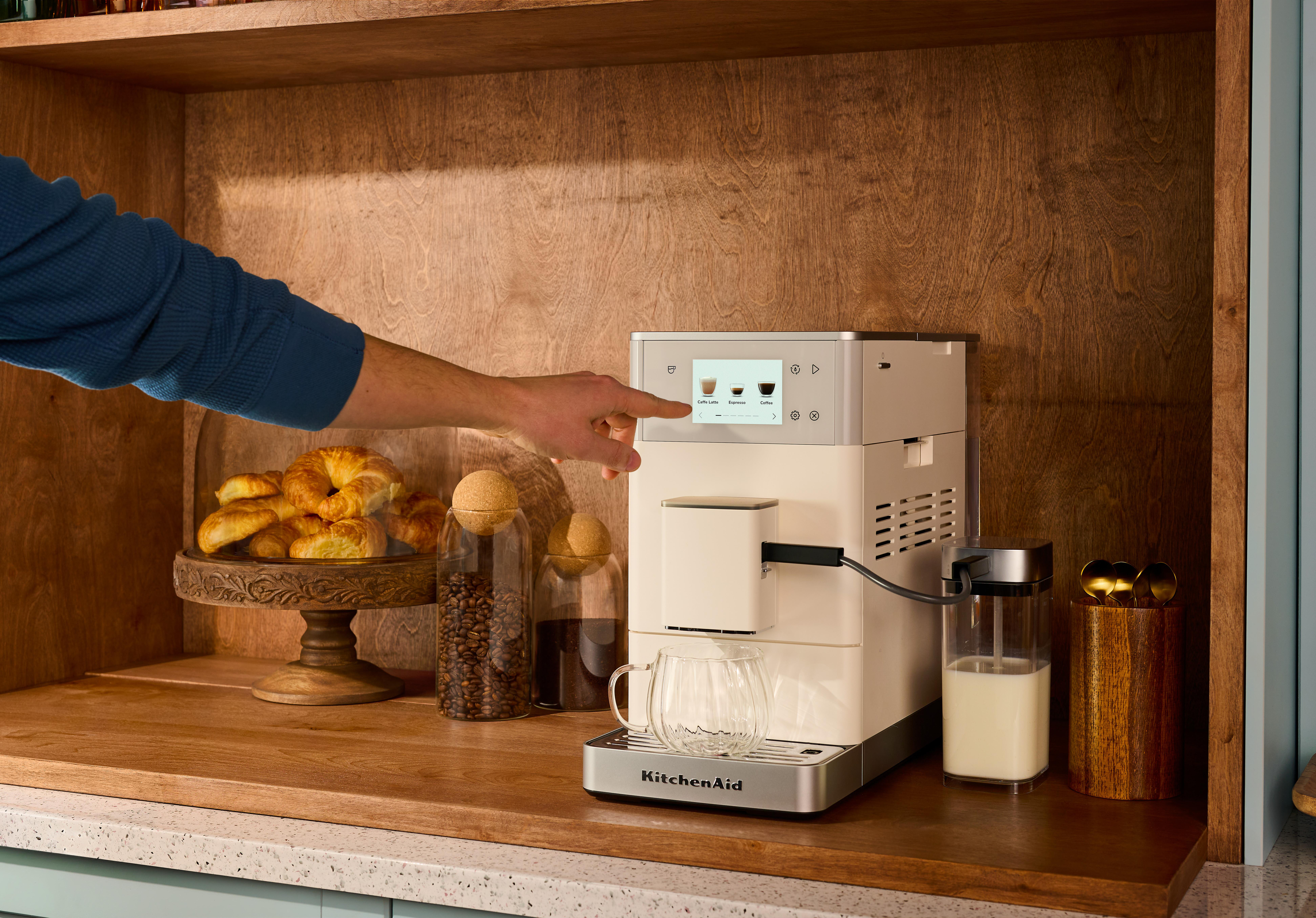 Eine Hand bedient eine Kaffeemaschine, daneben Croissants und Kaffeebohnen.