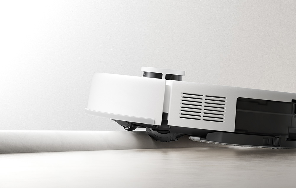 Biały robot sprzątający czyści białą krawędź ściany i podłogi.