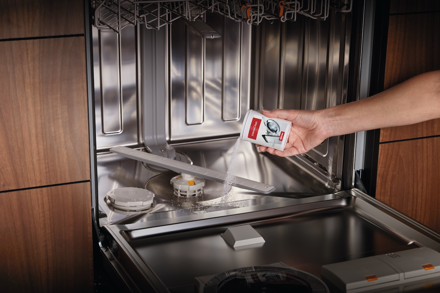Hand schüttet weißes Pulver aus Miele "IntenseClean" Behälter in offene Spülmaschine.