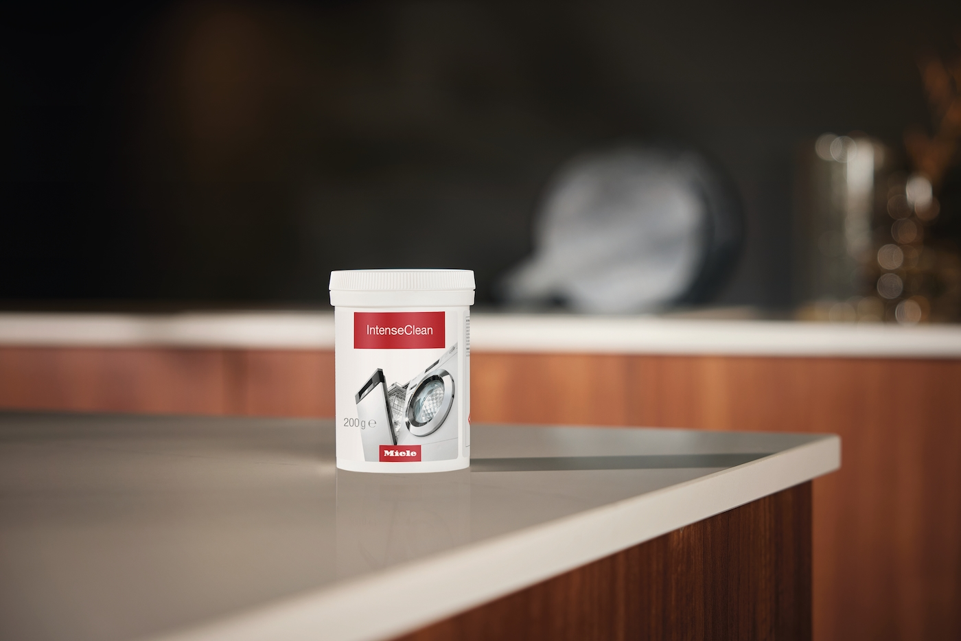 Ein weißer Behälter mit Miele IntenseClean Reinigungsmittel steht auf einer Arbeitsplatte.