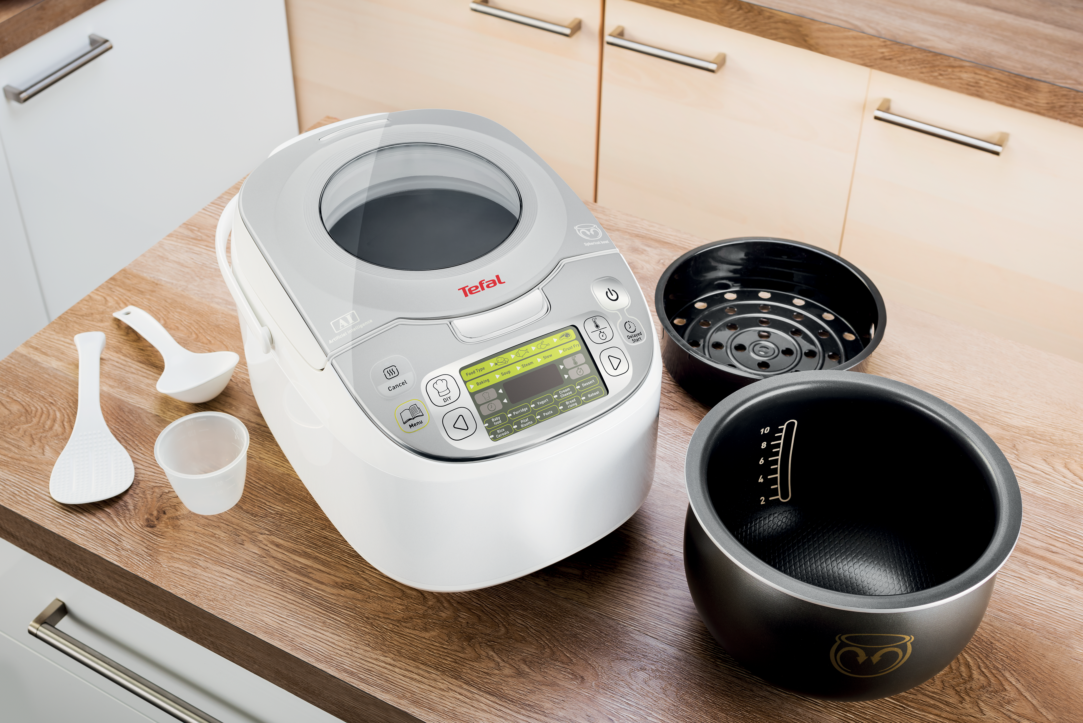 Fehér Tefal rizsfőző digitális kijelzővel, kiegészítőkkel körülvéve fa pulton.