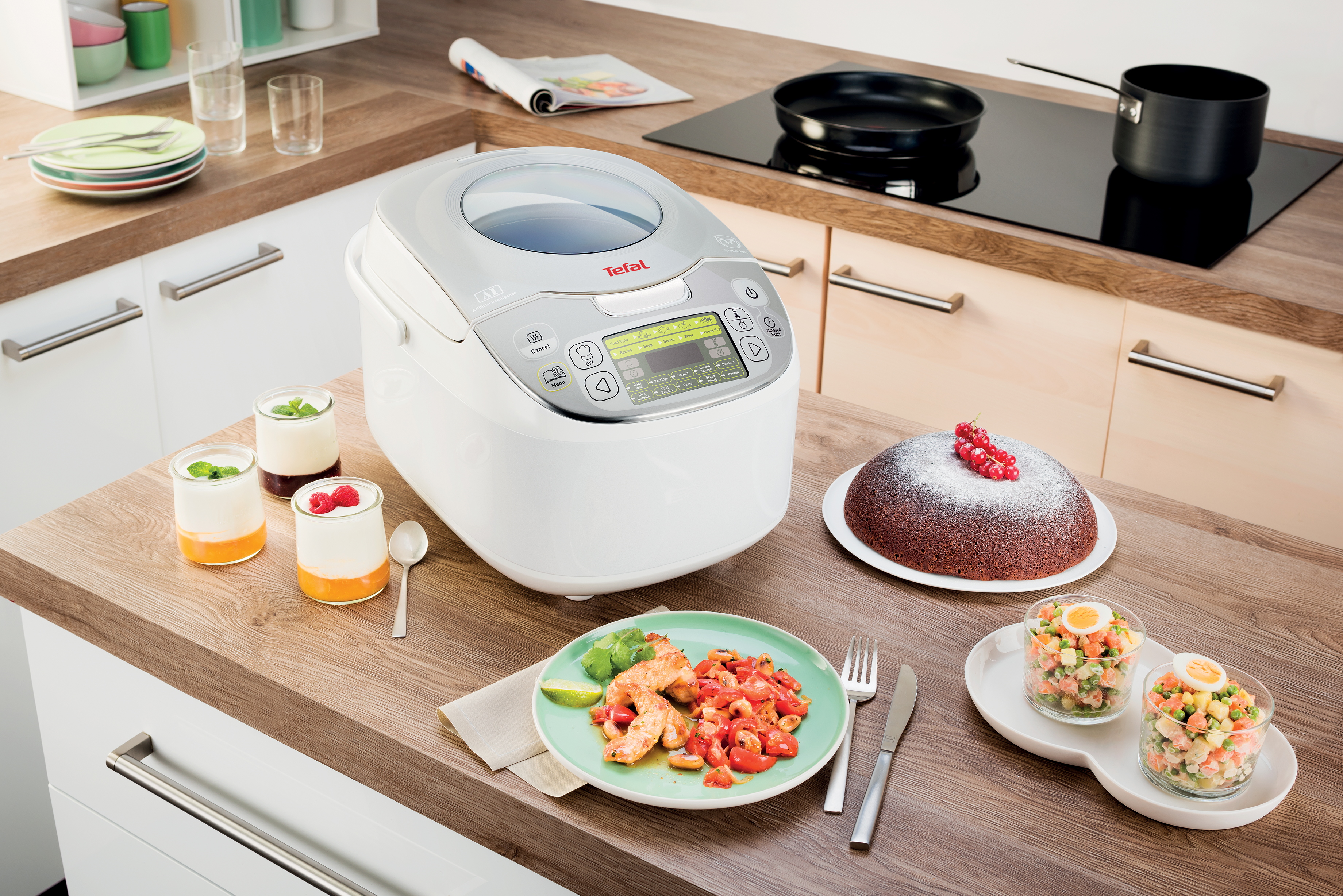 Egy Tefal multifunkciós főző a pulton áll, desszertek, garnélák és egy sütemény mellett.