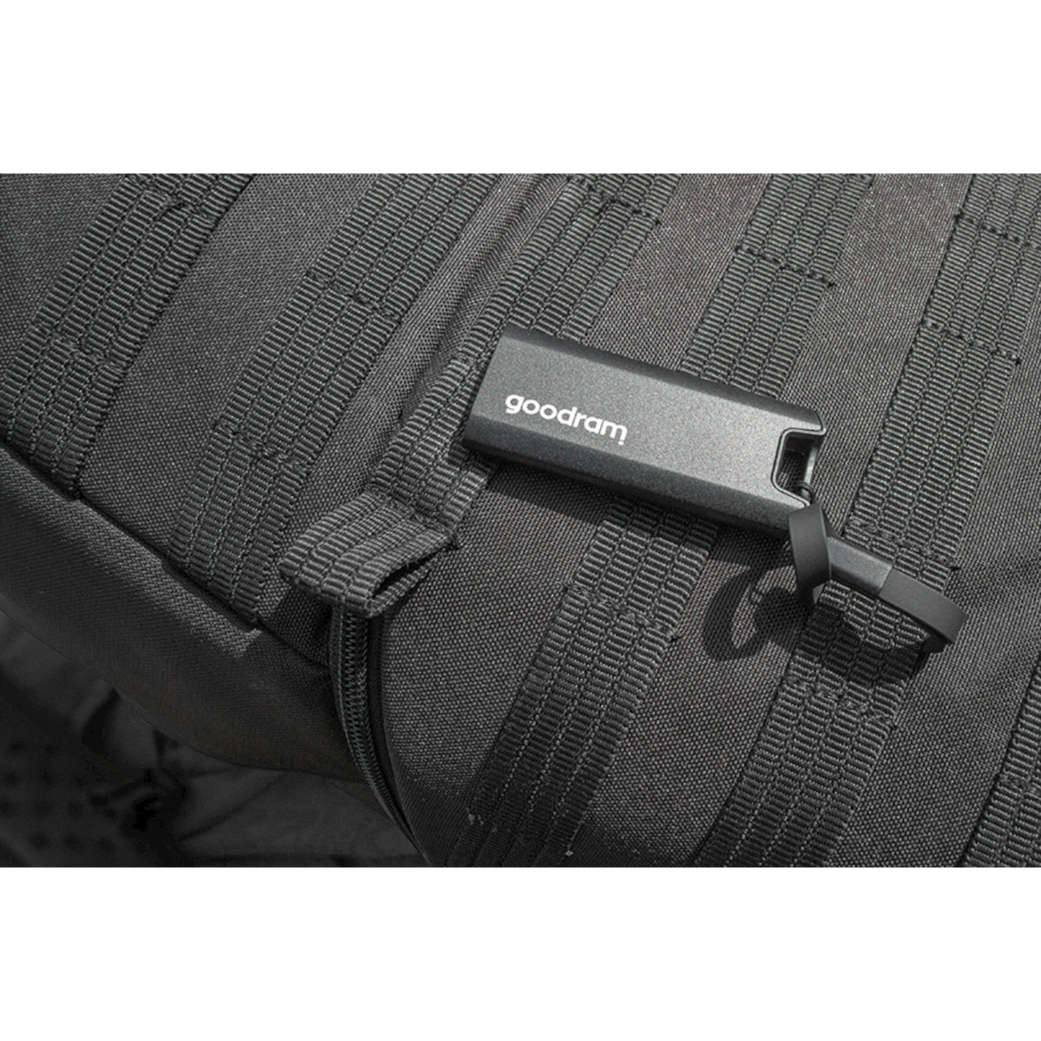Un'unità USB Goodram grigia attaccata a uno zaino tattico nero.