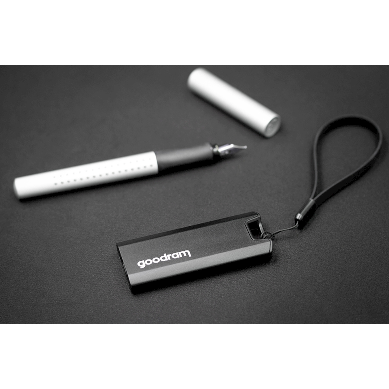Chiavetta USB Goodram nera con cinturino, penna e tappo su superficie scura.