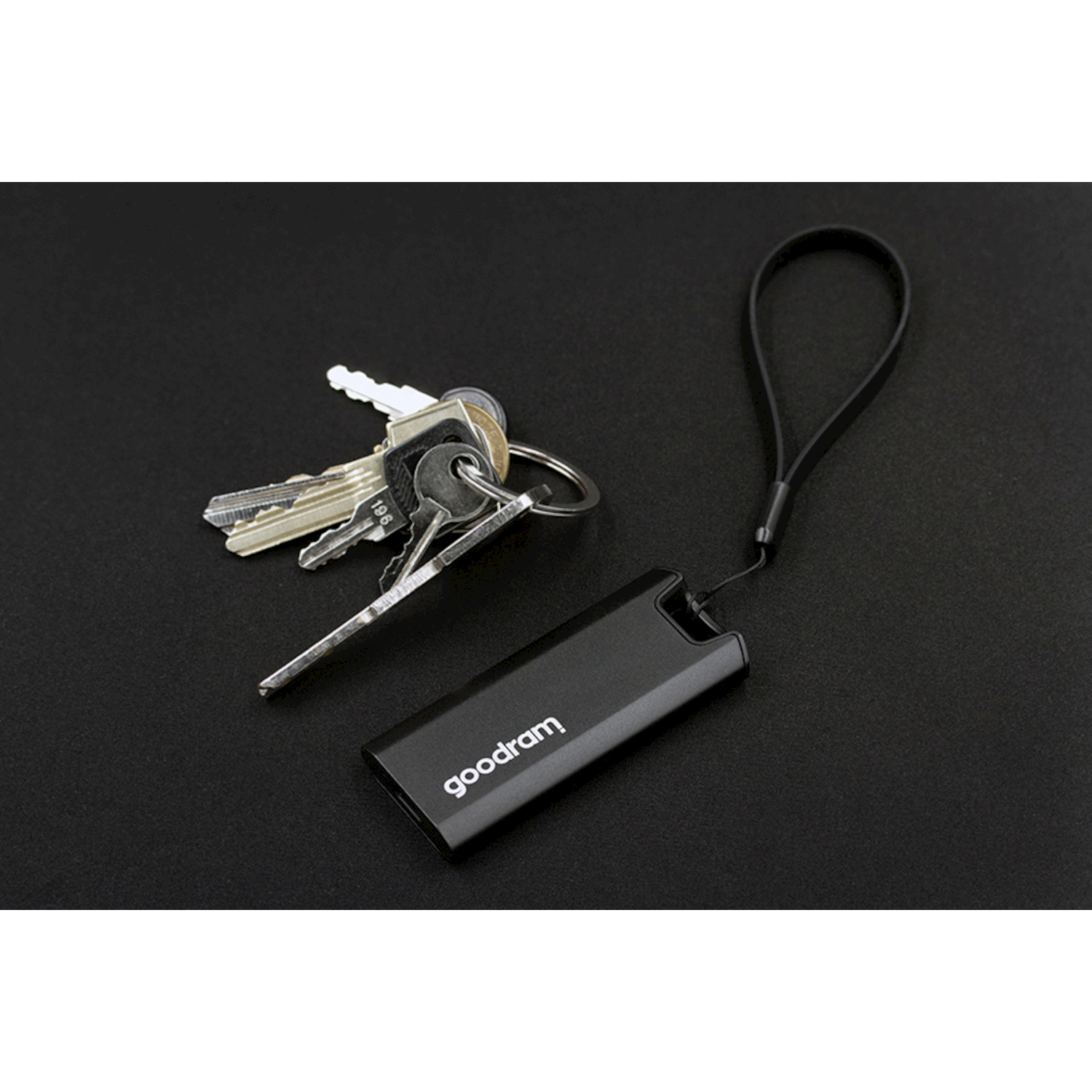 Un'unità USB nera con laccetto accanto a chiavi su superficie nera.