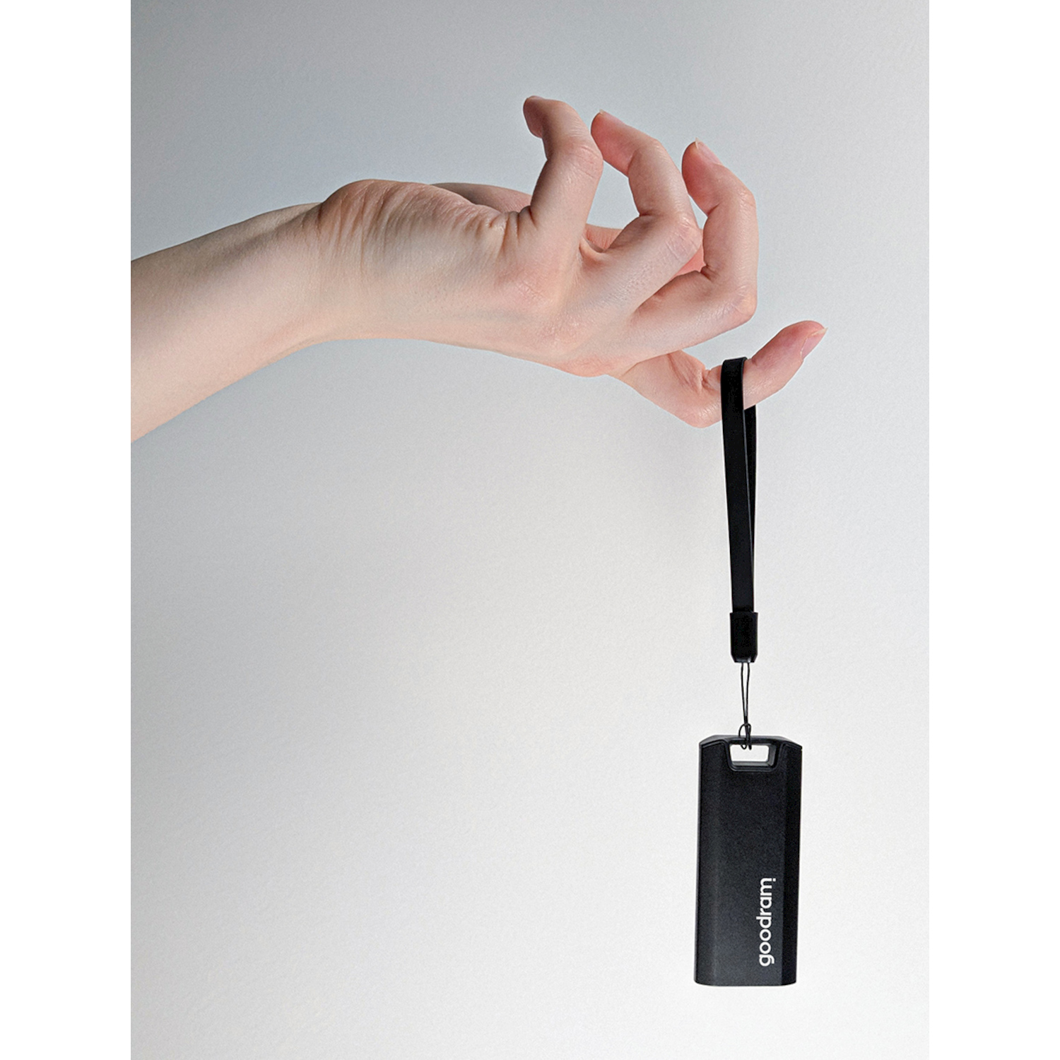 Una mano tiene una chiavetta USB nera con un cordino.
