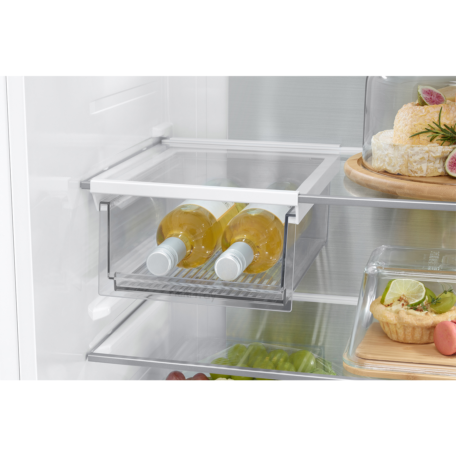 Dos botellas de vino en un cajón de refrigerador junto a quesos y tartas de frutas.