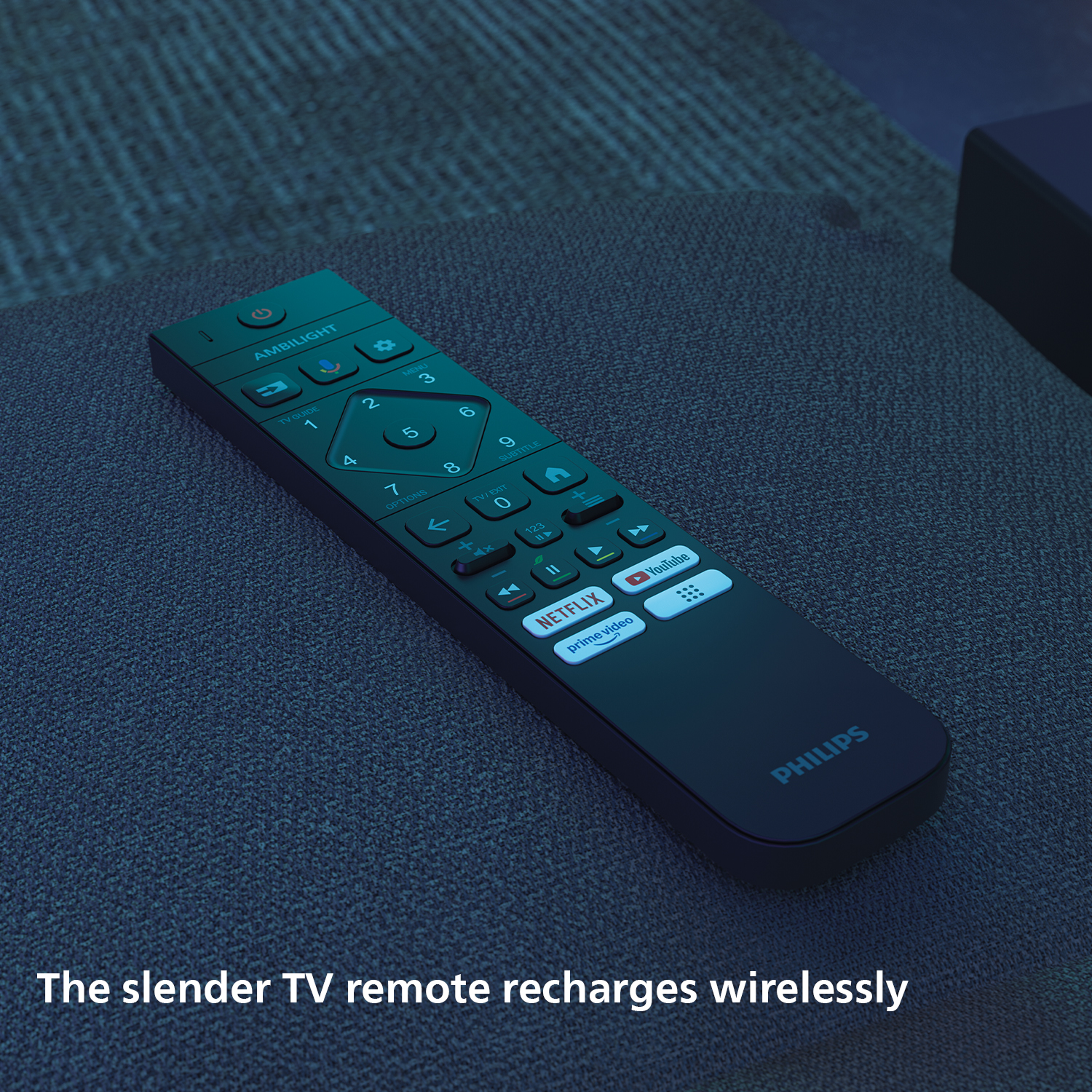 Czarny pilot TV Philips z przyciskiem Ambilight leży na ciemnej tkaninie.