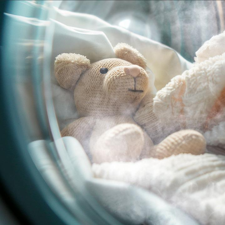 Un oso de peluche yace en una lavadora sobre ropa blanca.