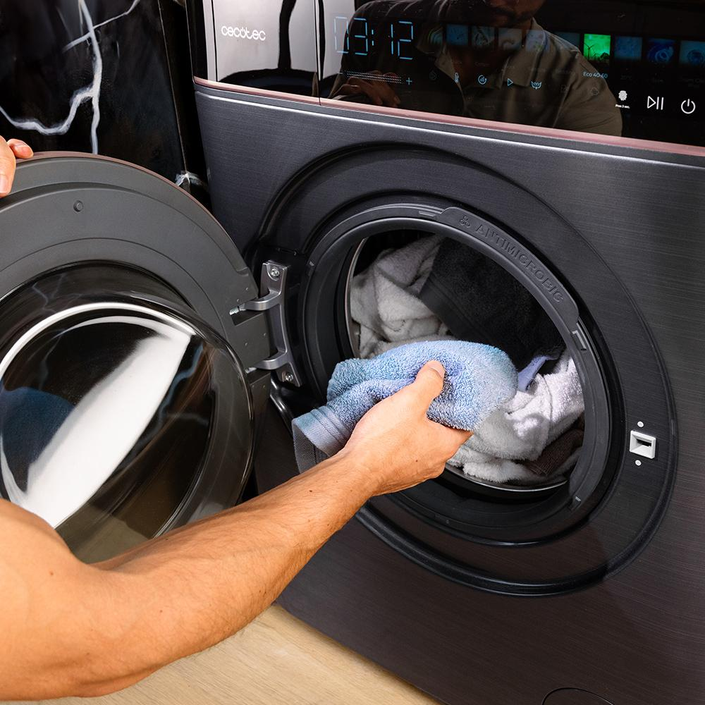 Una mano mete una toalla azul en una lavadora abierta con ropa.