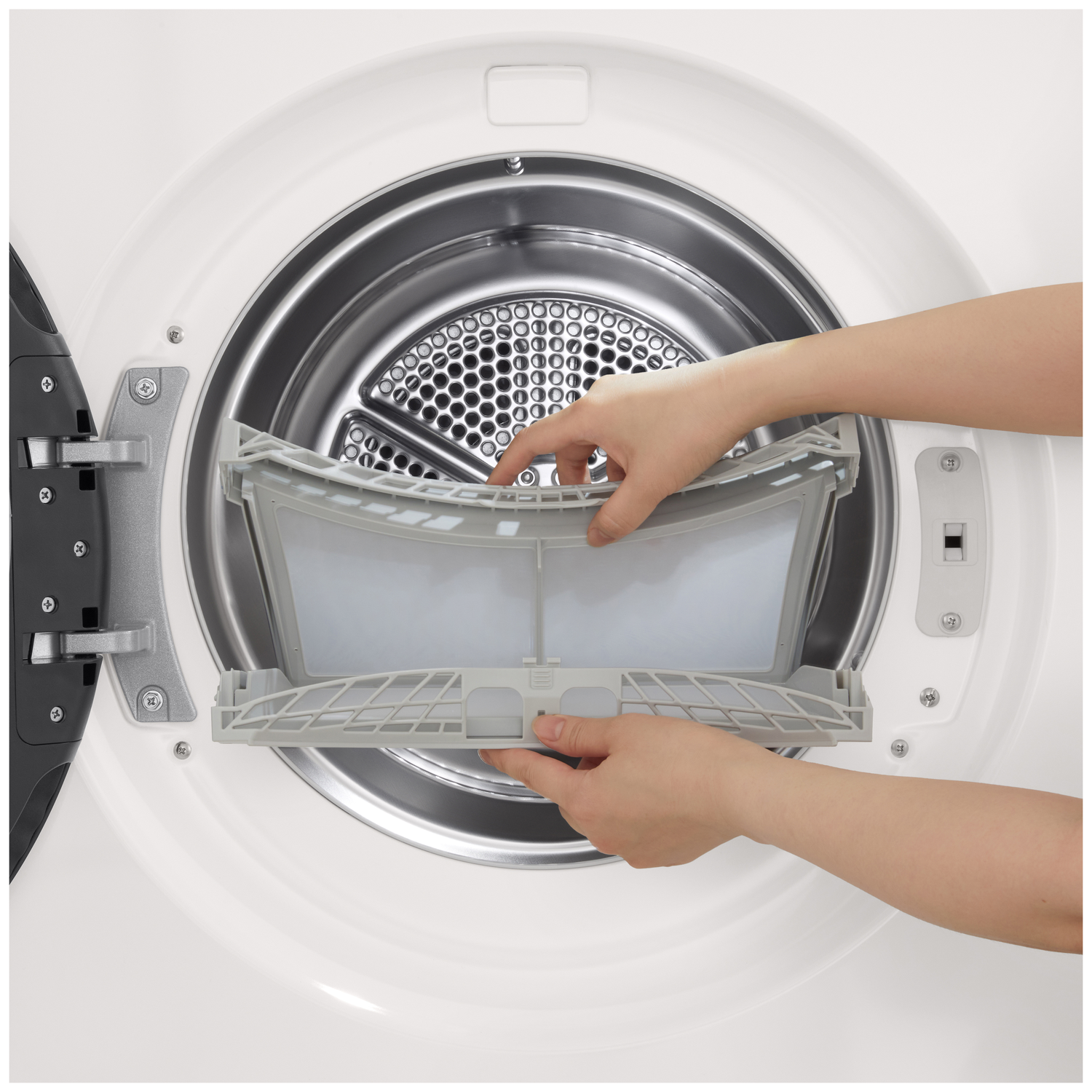 Een persoon verwijdert een grijs pluizenfilter uit een witte wasmachine.