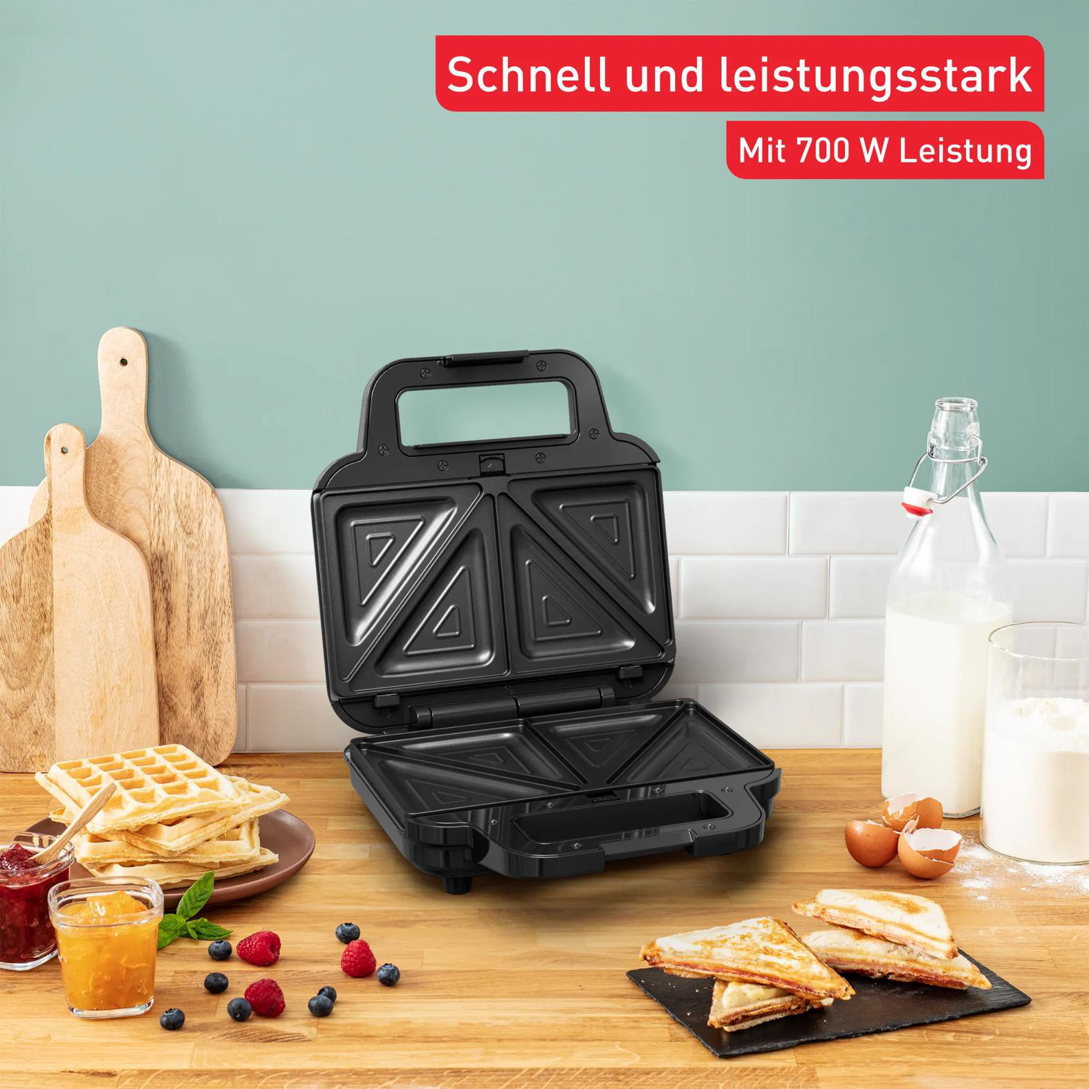 Ein offener schwarzer Sandwichmaker mit Waffeln, Toast und Zutaten.