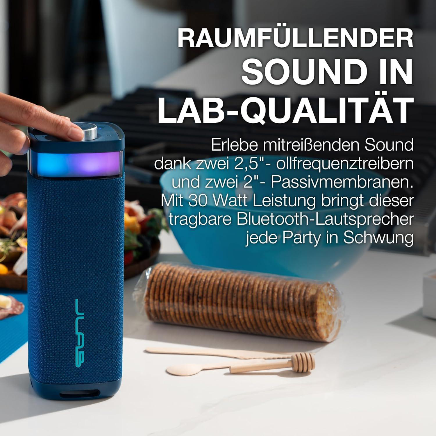 Ein blauer JLab Bluetooth-Lautsprecher mit bunten Lichtern steht neben Snacks.
