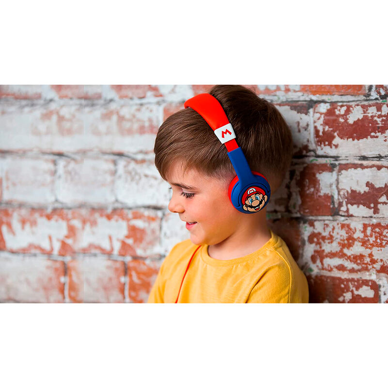Niño con auriculares rojos y azules de Mario frente a una pared de ladrillos.