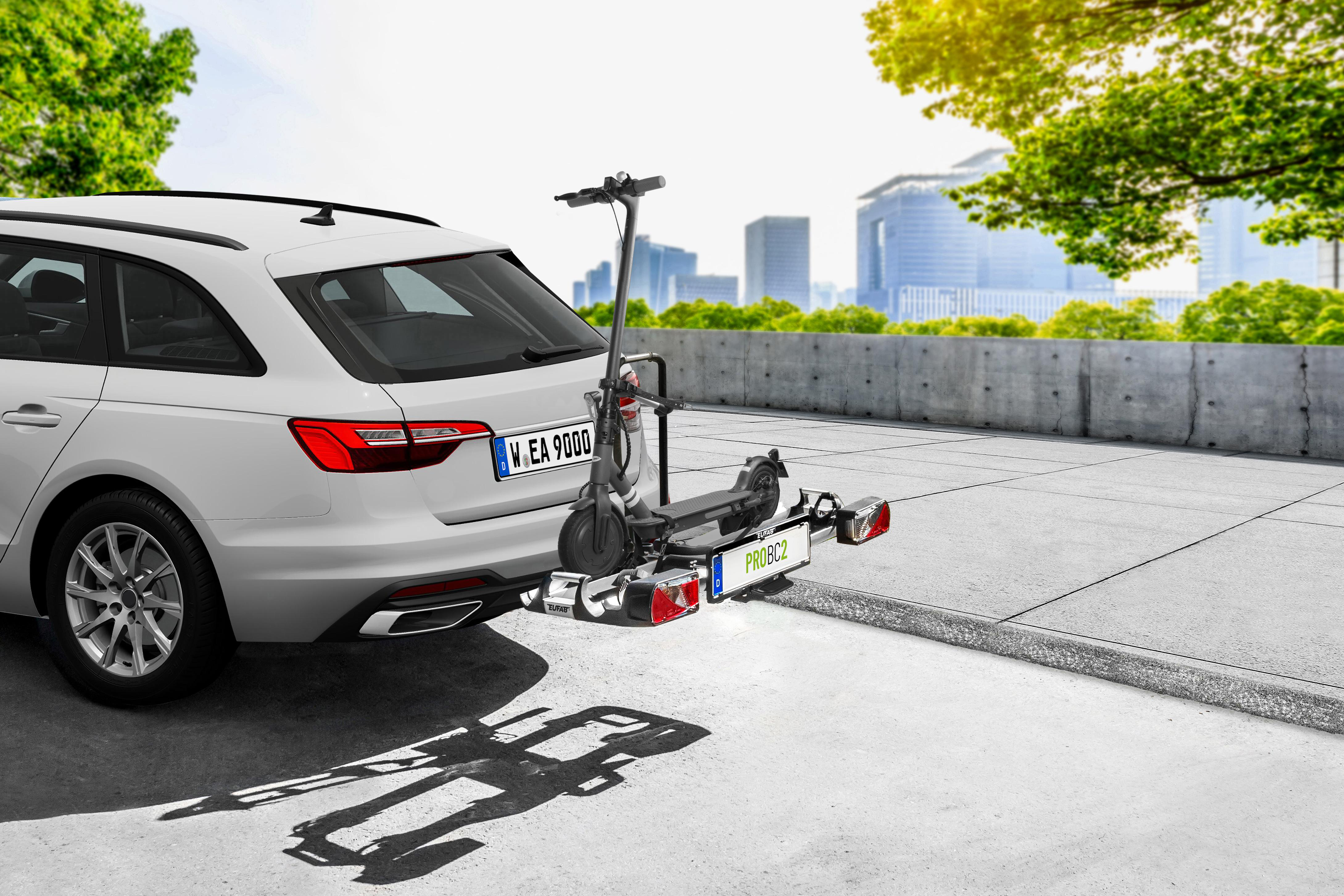 Ein weißer Kombi mit E-Scooter auf einem Fahrradträger, städtische Kulisse.