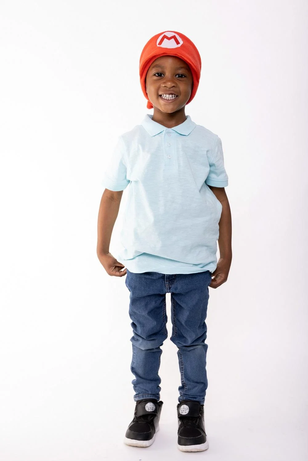 Un niño con gorro rojo de Mario y polo azul claro frente a un fondo blanco.
