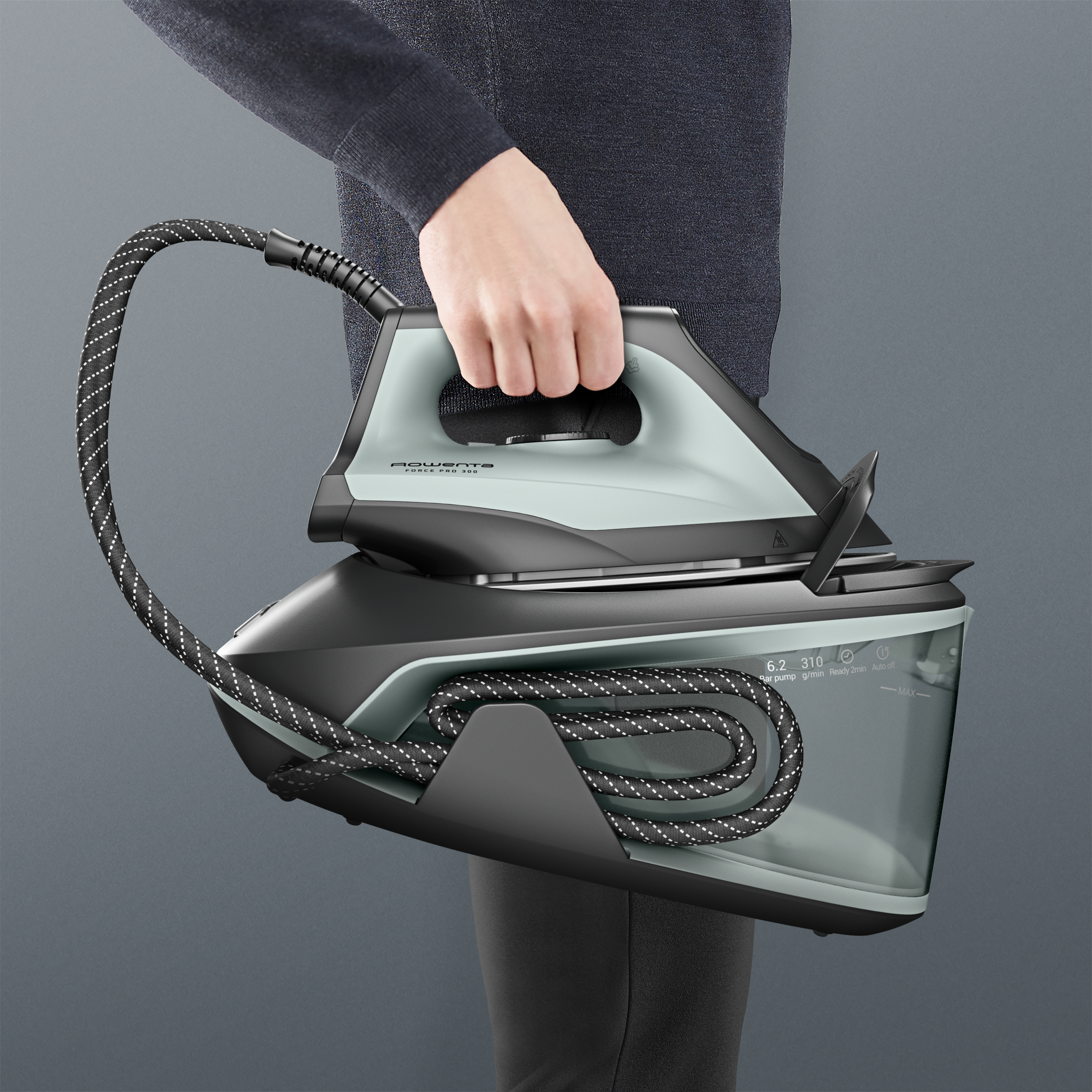 Una persona sostiene una plancha de vapor azul verdoso con cable negro.