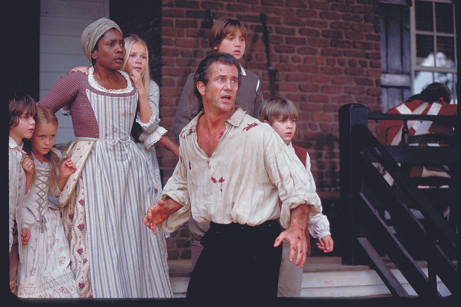 Eine Gruppe von Menschen, darunter Mel Gibson, steht vor einem Backsteinhaus.
