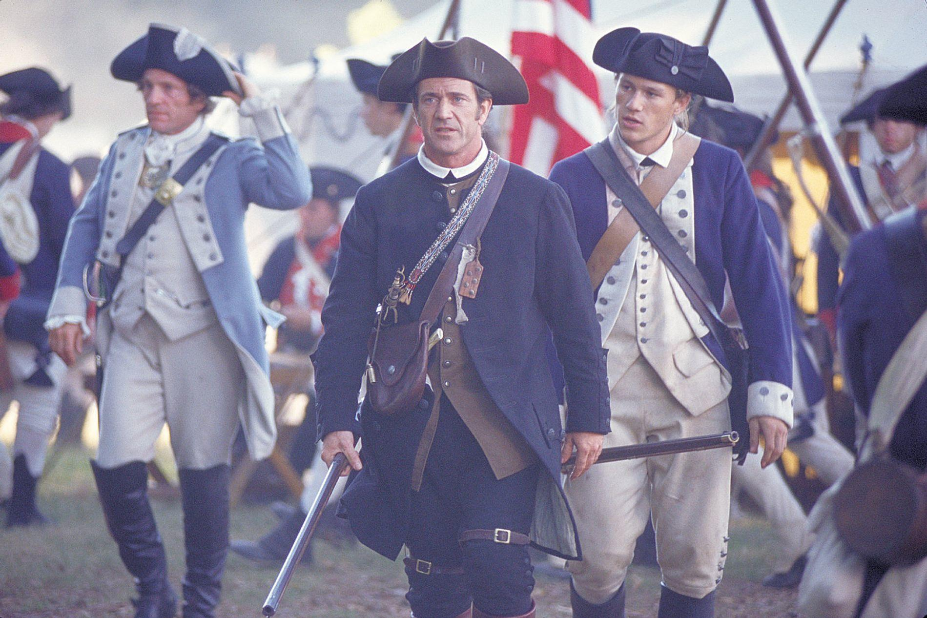 Männer in historischen Uniformen mit Hüten, die Gewehre tragen, marschieren.