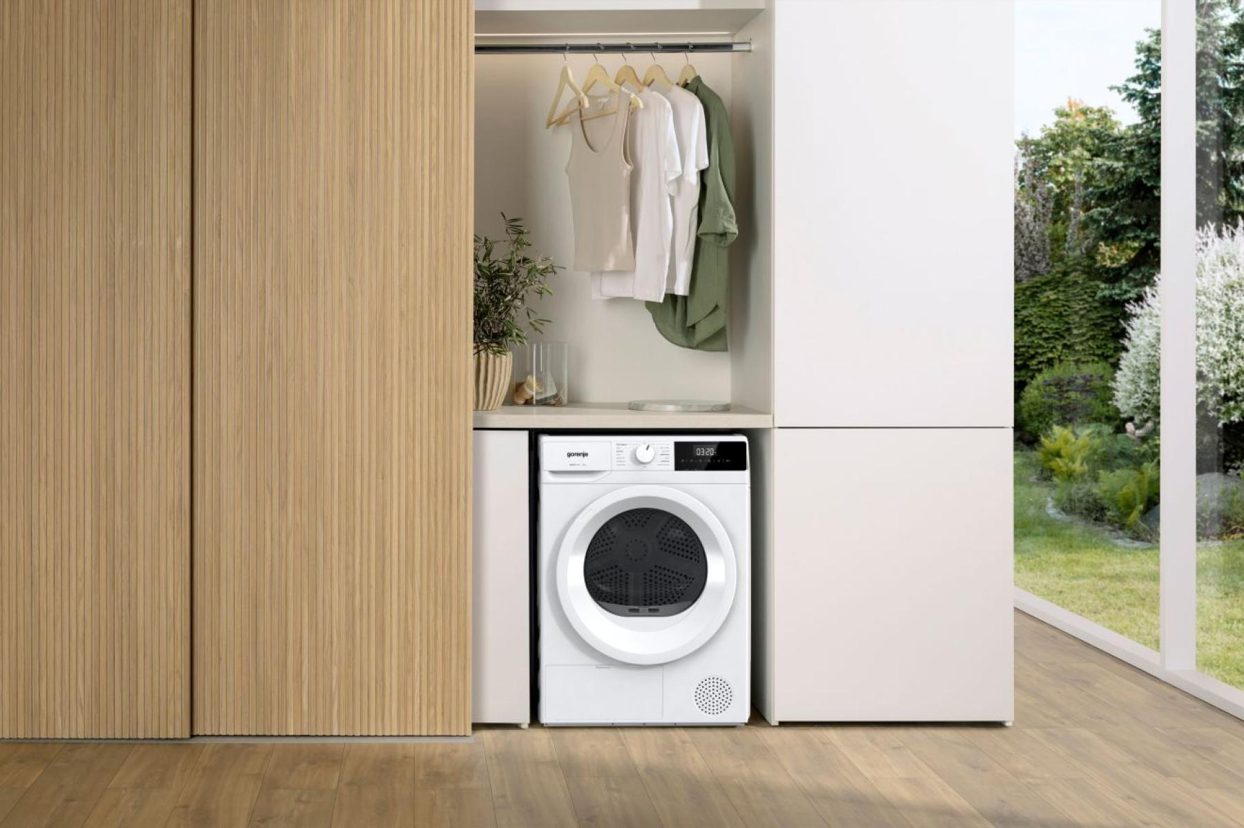 Ein weißer Trockner steht neben einem Kleiderschrank mit Kleiderbügeln und Kleidung.