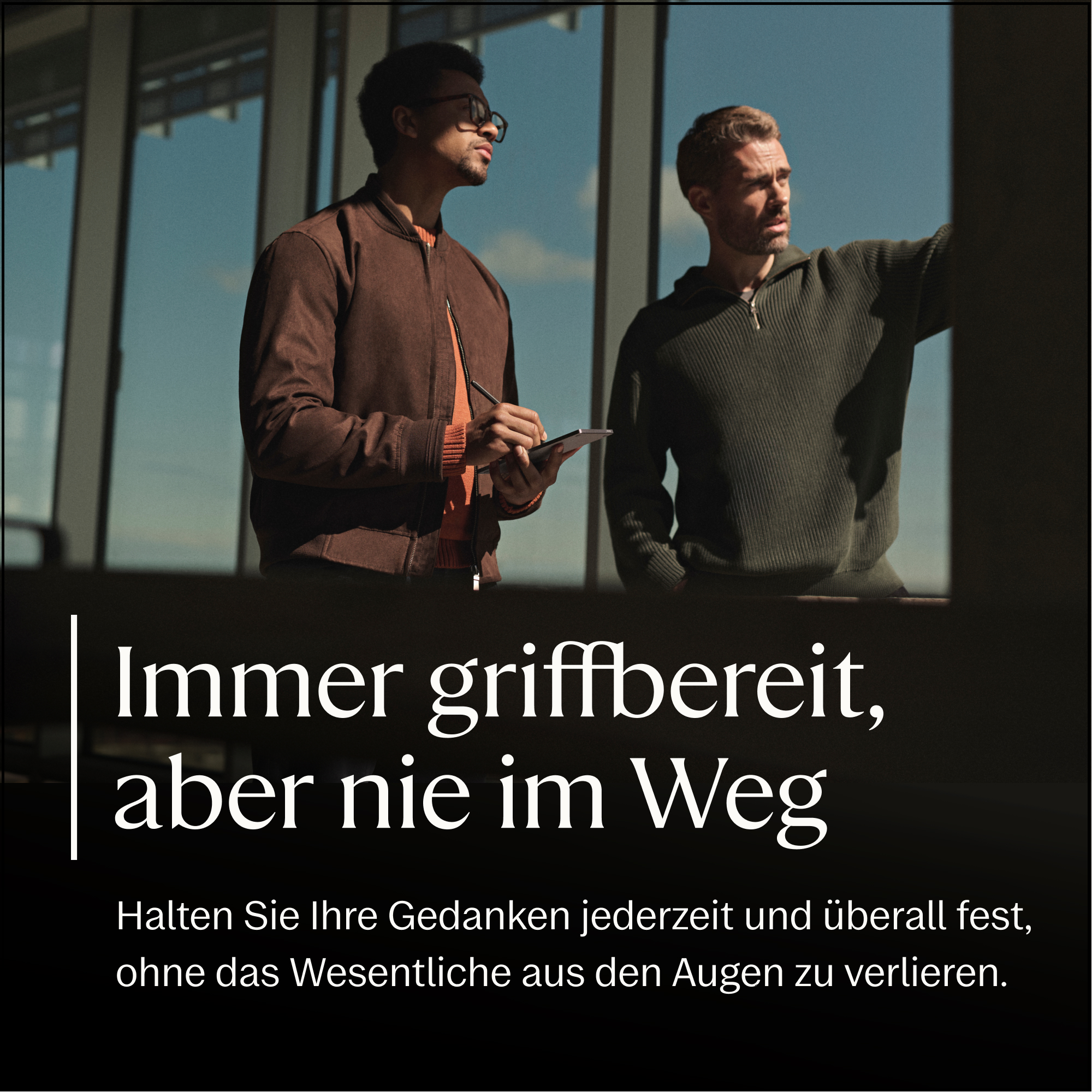 Zwei Männer stehen vor einem Fenster. Einer schreibt auf einem Tablet.