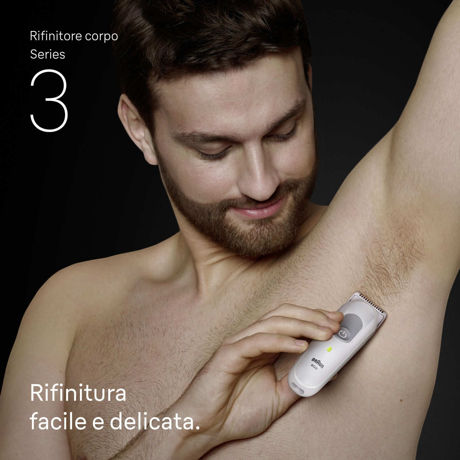 Uomo che si rade l'ascella con rifinitore bianco. Sfondo scuro.