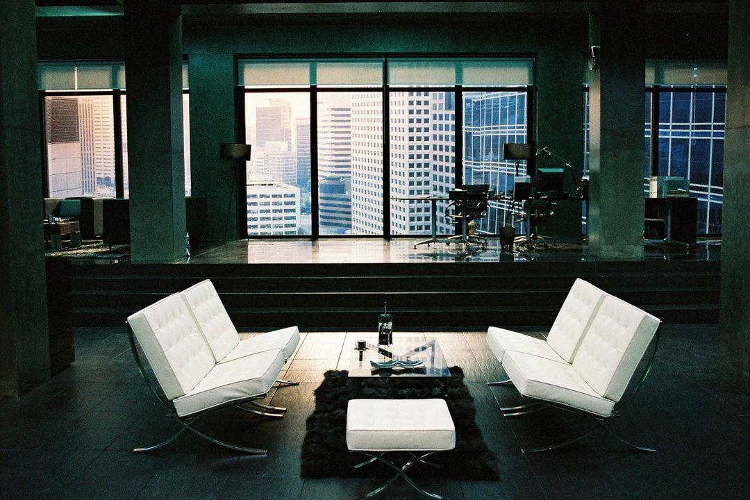 Moderne Lounge mit weißen Sesseln, Glastisch und Stadtblick durch große Fenster.