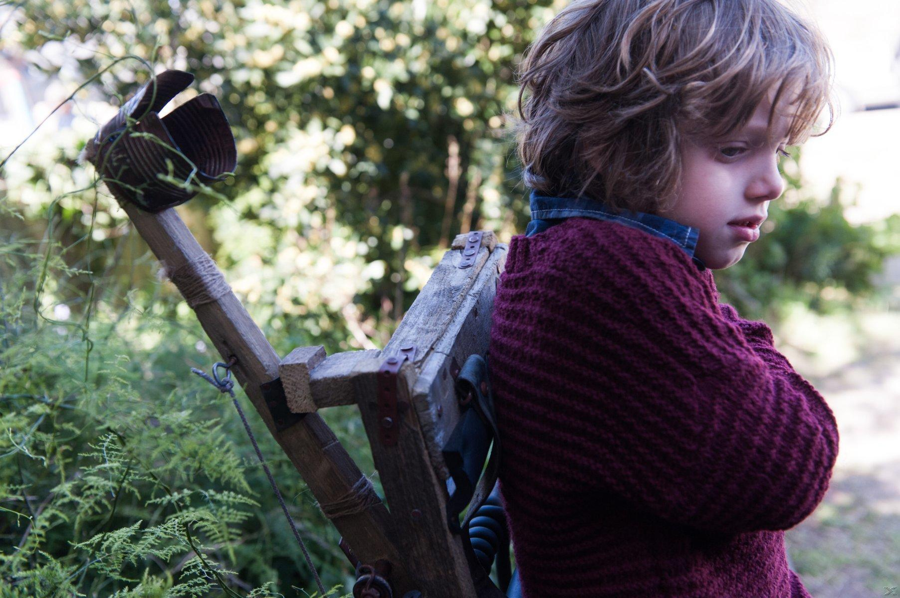 Ein Kind mit einem Strickpullover steht neben einem Holzgestell im Freien.