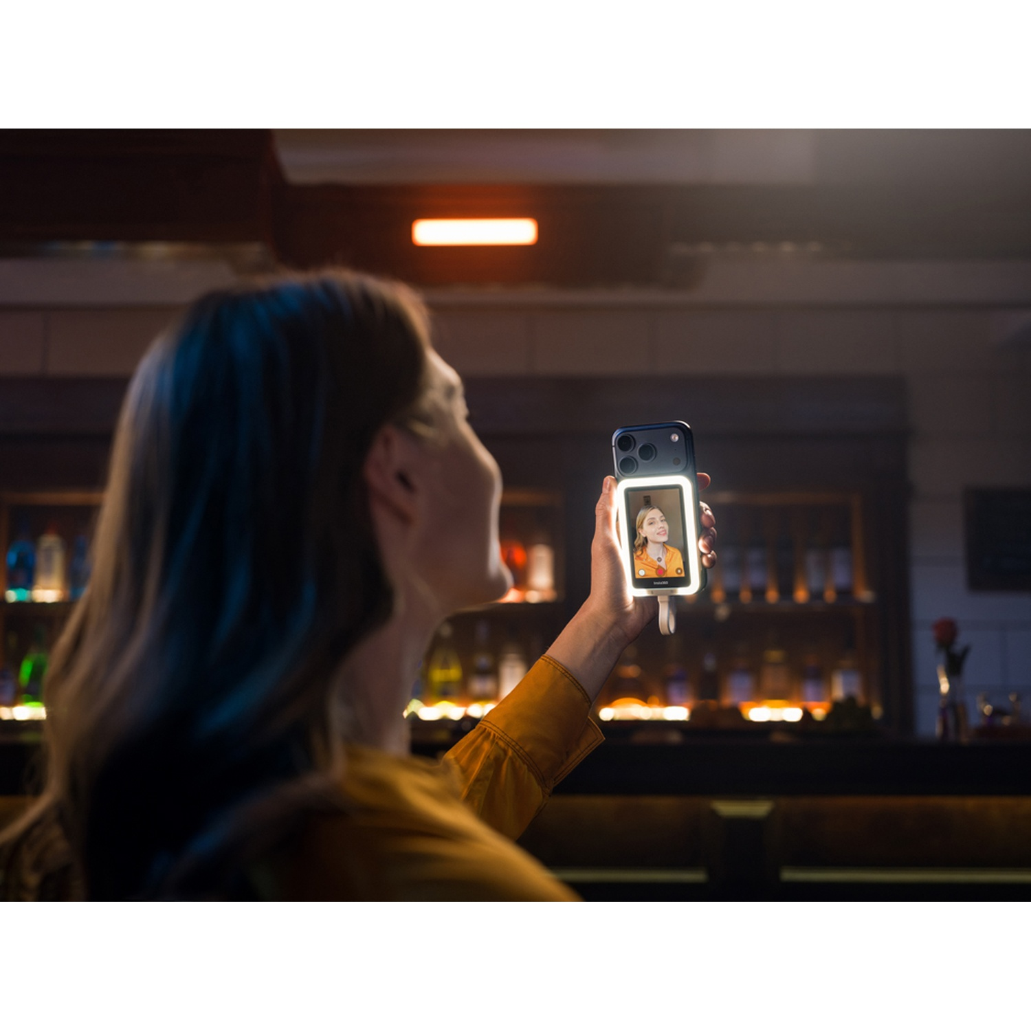 Una donna si scatta un selfie con un telefono illuminato in un bar.