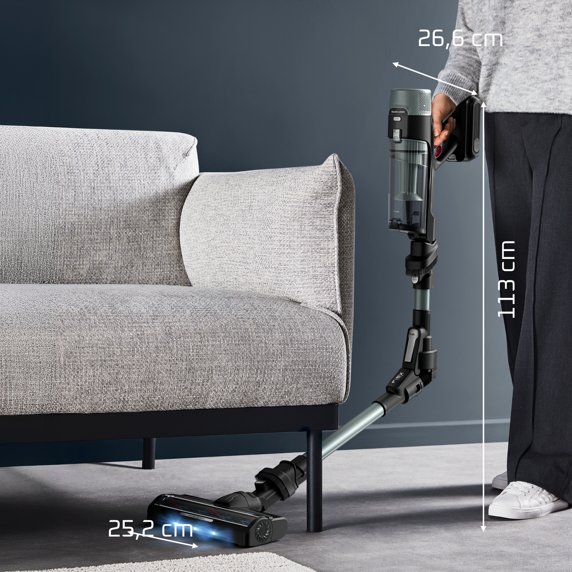 Ein Akkustaubsauger mit flexibler Düse reinigt unter einem grauen Sofa.