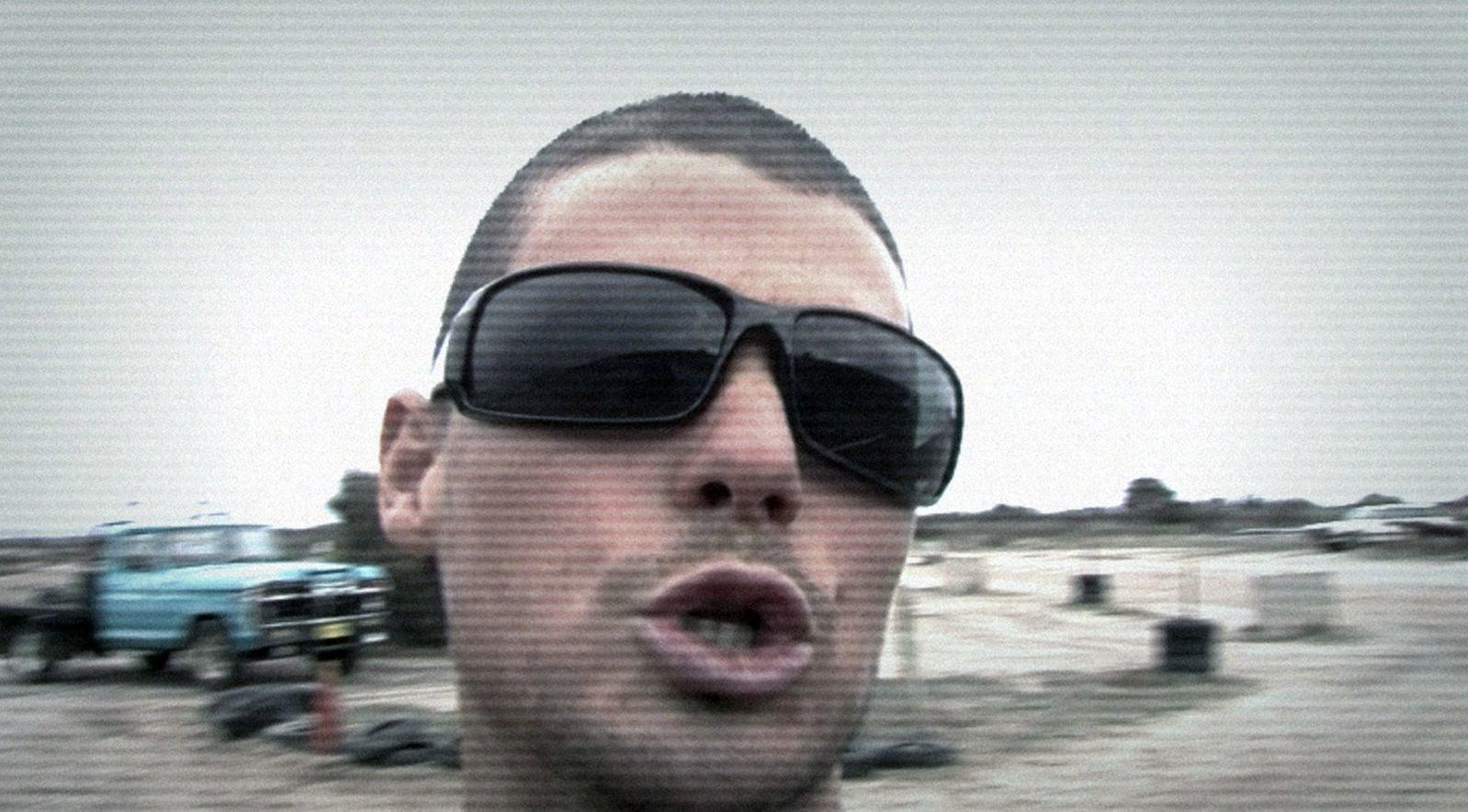 Ein Mann mit Sonnenbrille spricht vor einem blauen Lastwagen.