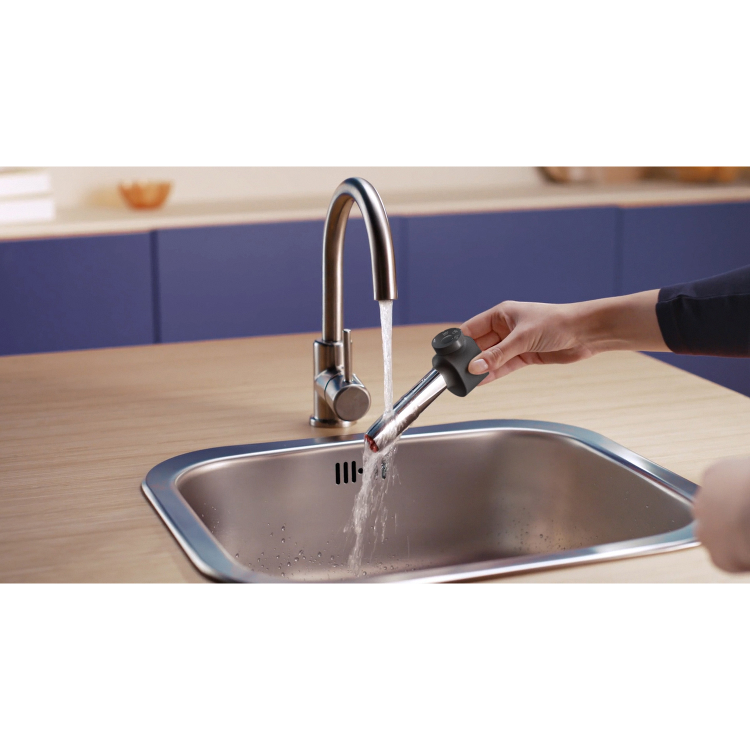 Een hand houdt een zwarte opzetstuk onder stromend water in een gootsteen.