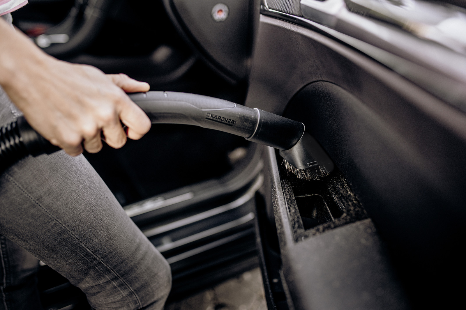 Osoba odkurza wnętrze samochodu szczotką.