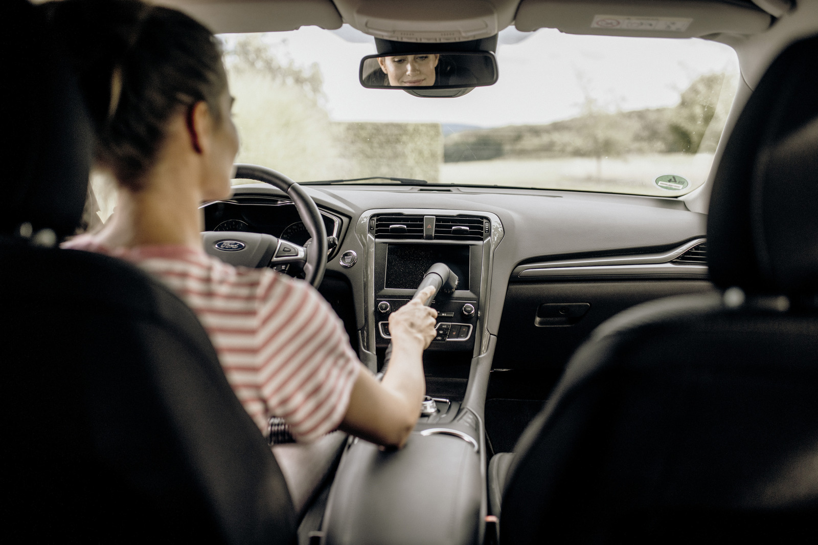 Kobieta w samochodzie czyści ekran odkurzaczem.