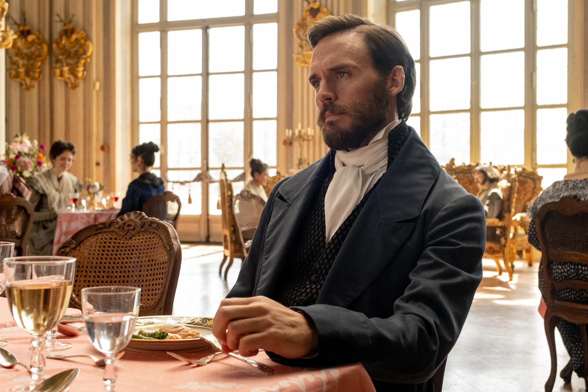 Mann in historischer Kleidung sitzt an einem gedeckten Tisch in einem eleganten Raum.