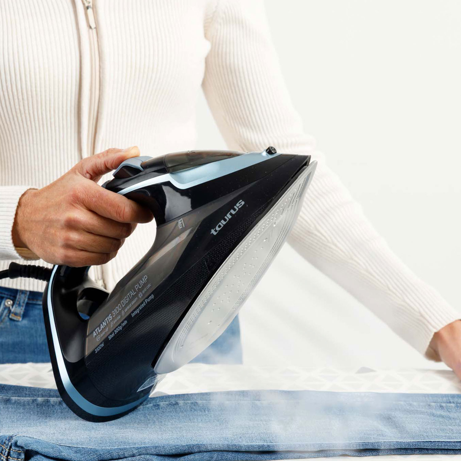 Una persona plancha unos vaqueros azules con una plancha de vapor negra y azul.